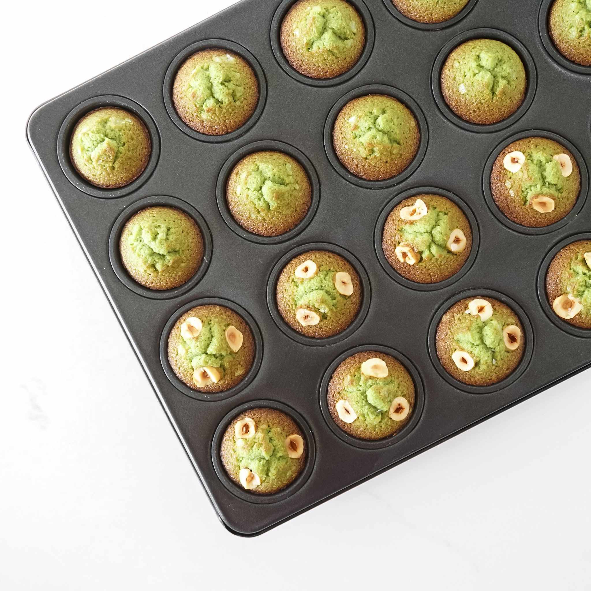 Mini muffin tray with green muffins on a white background