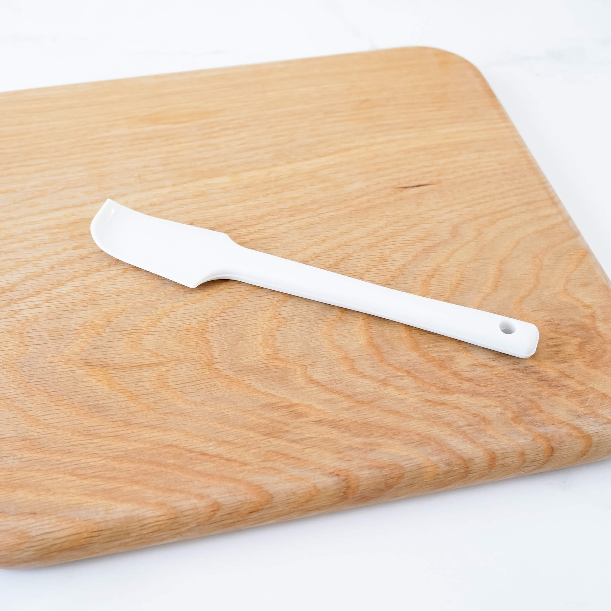 A white silicone spatula on a wooden cutting board.