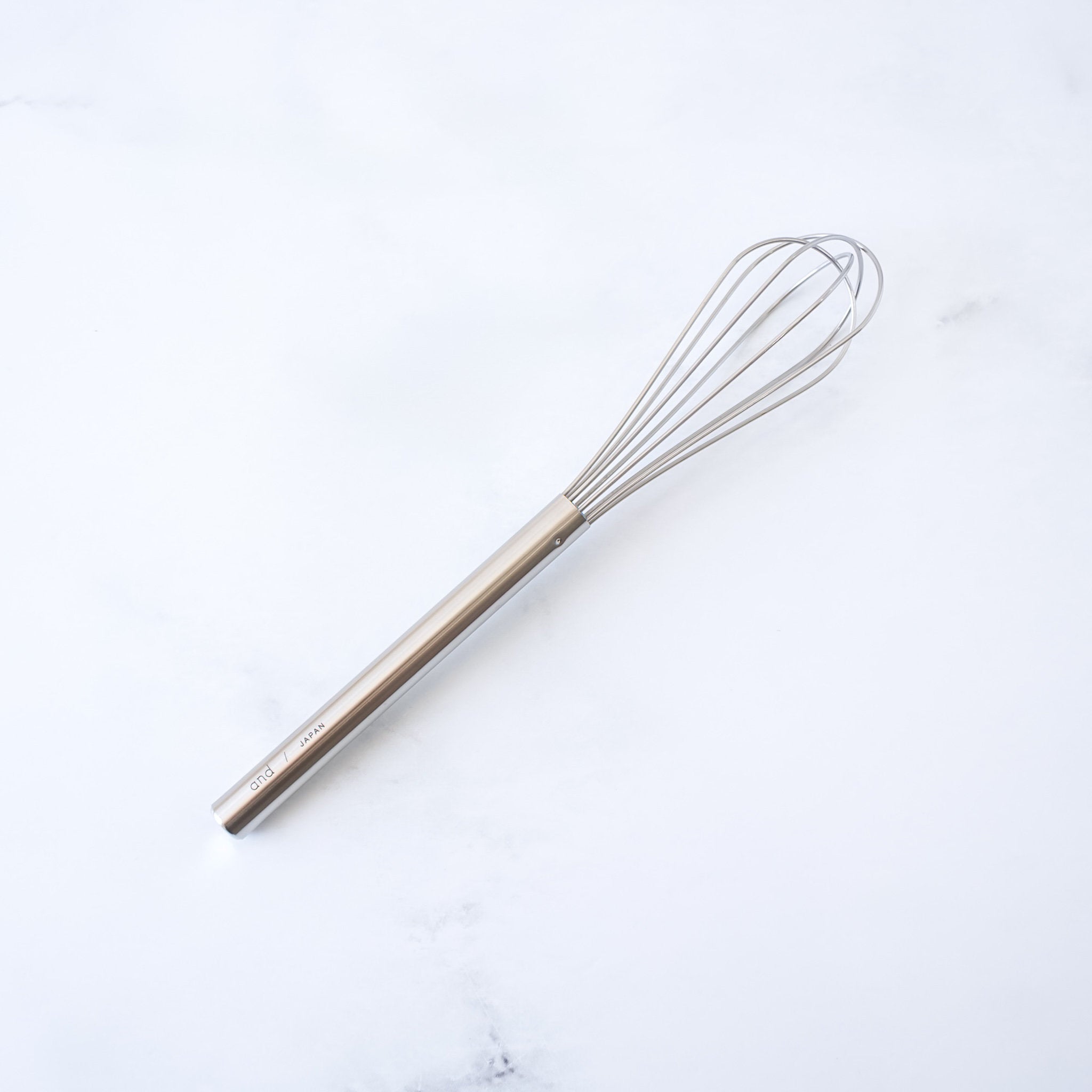 Stainless steel mini whisk on a white marble surface