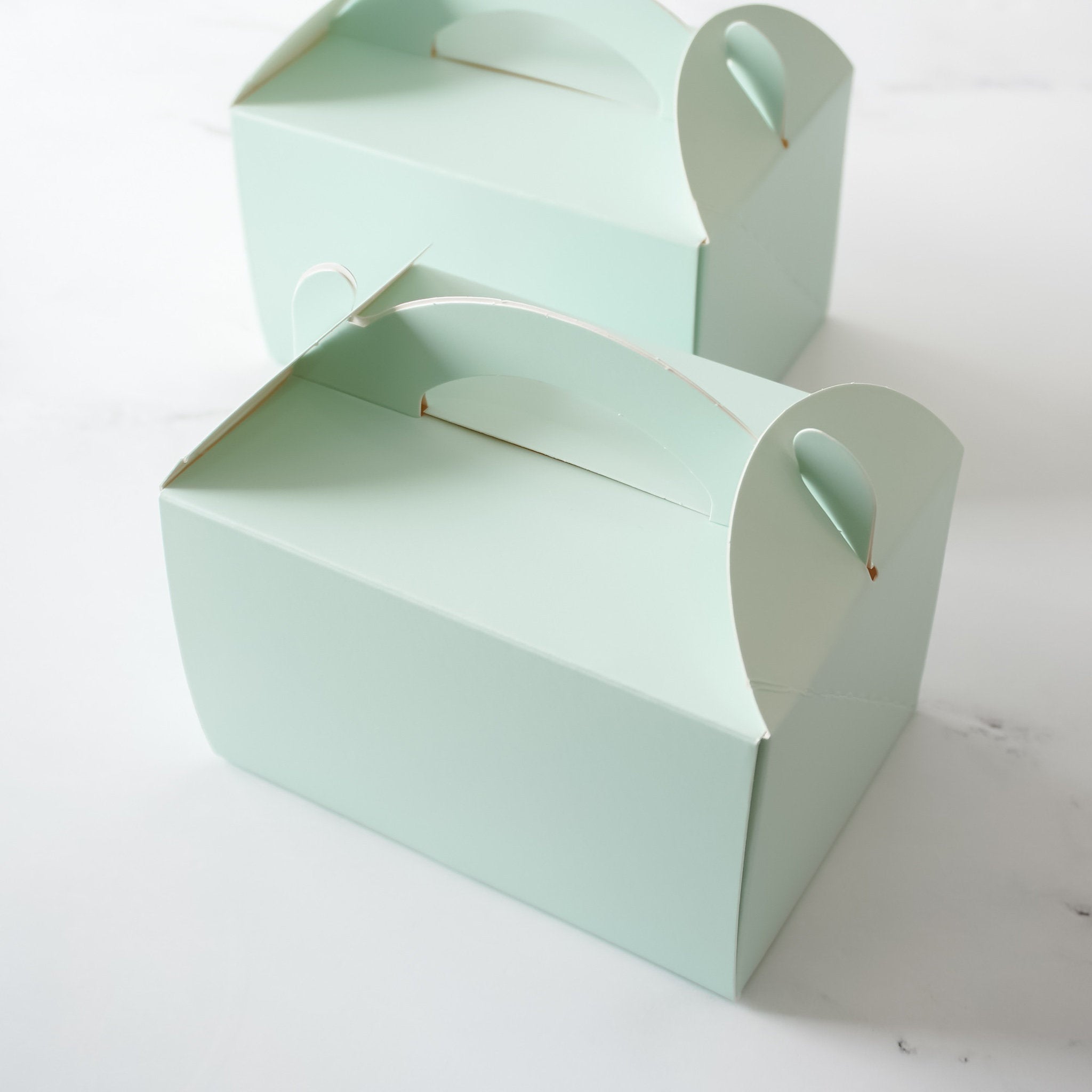 Two light green cardboard boxes with cut-out handles. The boxes are stacked on top of each other.