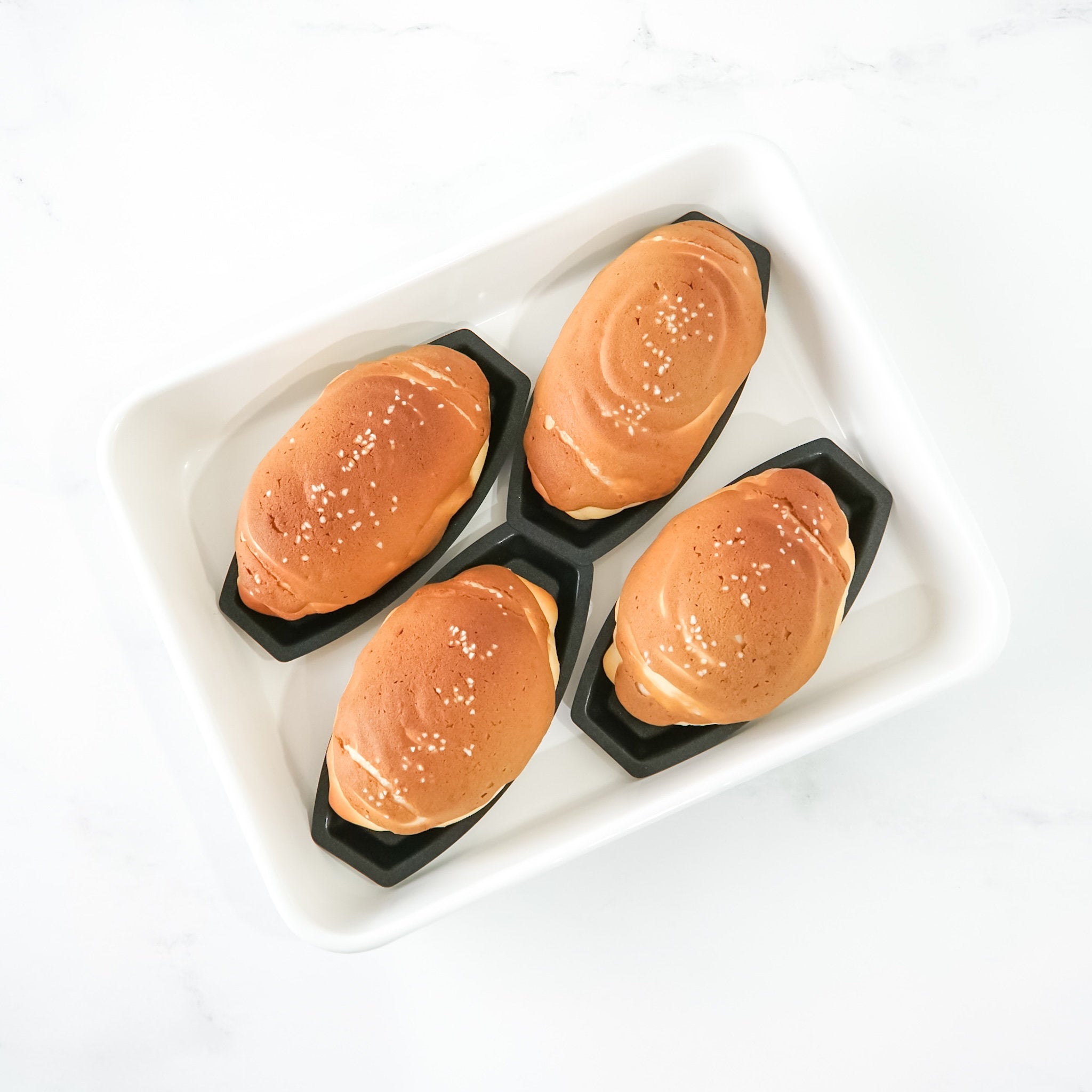 Four roti boy buns in black salt bread pans on a white tray