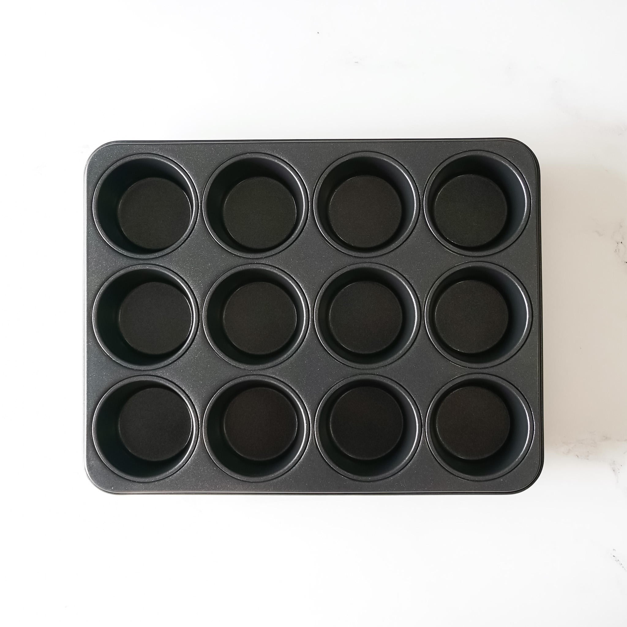 A black metal muffin pan with 12 individual round cavities. The tin is empty and ready for baking.