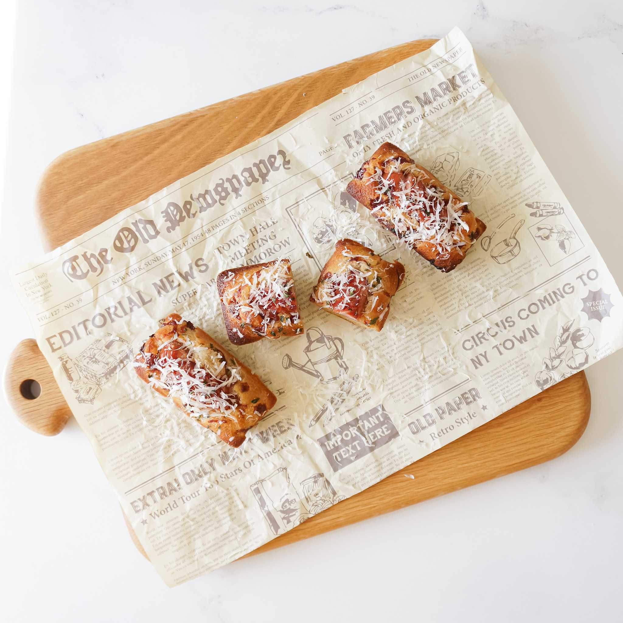 Four small, square, baked goods with a brown crust and white cheese topping on a white paper with text that reads &