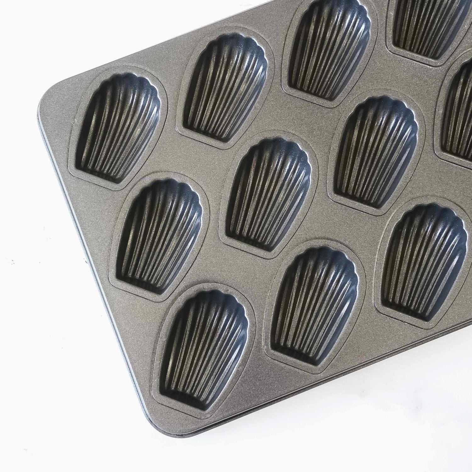 A black metal baking pan with 12 individual molds shaped like seashells. The pan is designed for baking madeleines.