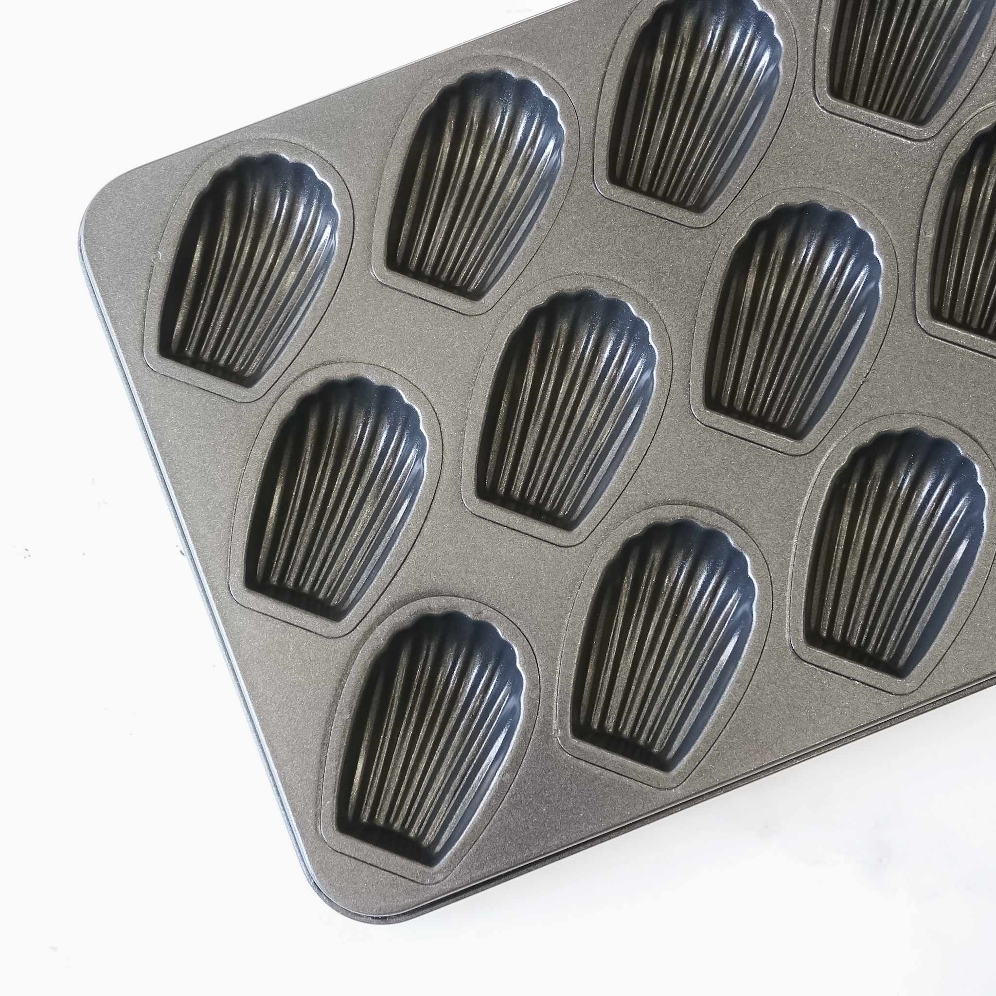 A black metal baking pan with 12 individual molds shaped like seashells. The pan is designed for baking madeleines.