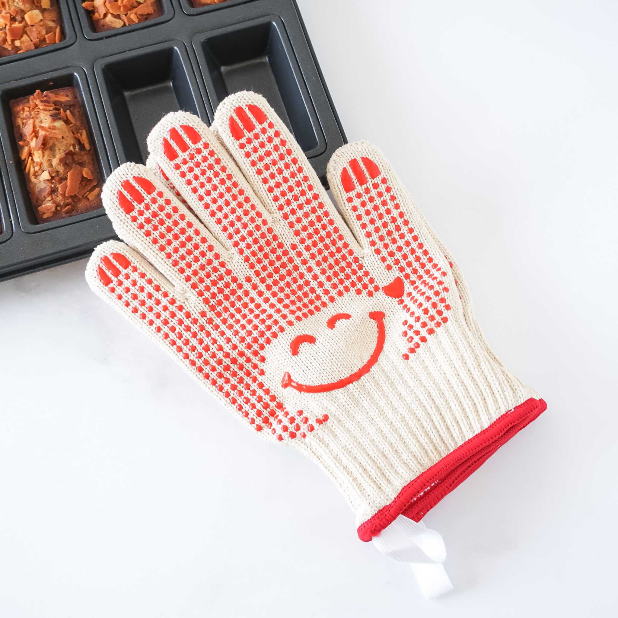 White oven mitt with red textured grip and smiley face design on a white background