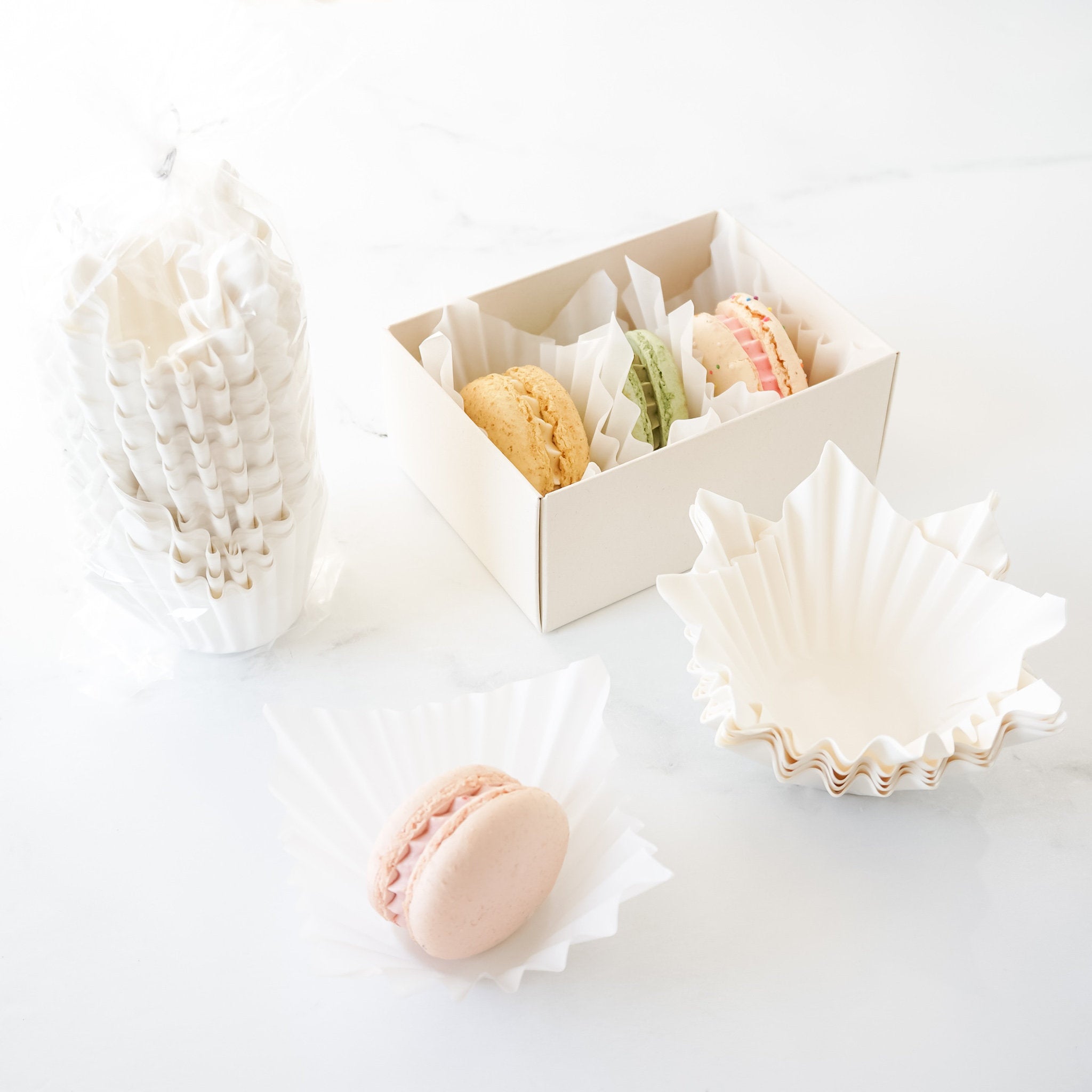 White fluted cupcake liners displayed alongside a box of macarons, with one liner placed inside a cupcake holder.