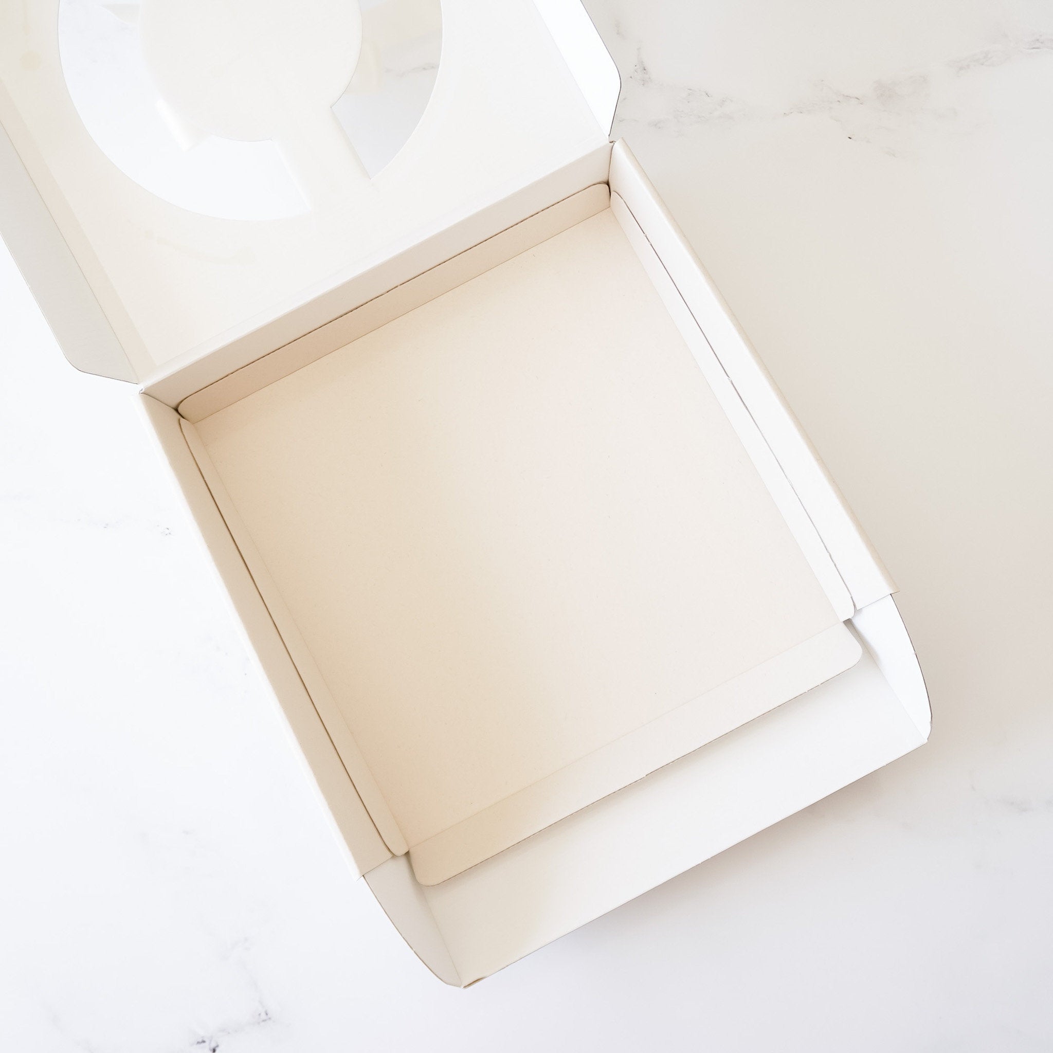 A light beige cardboard box with a clear plastic window on the top. The box is open and the inside is empty.