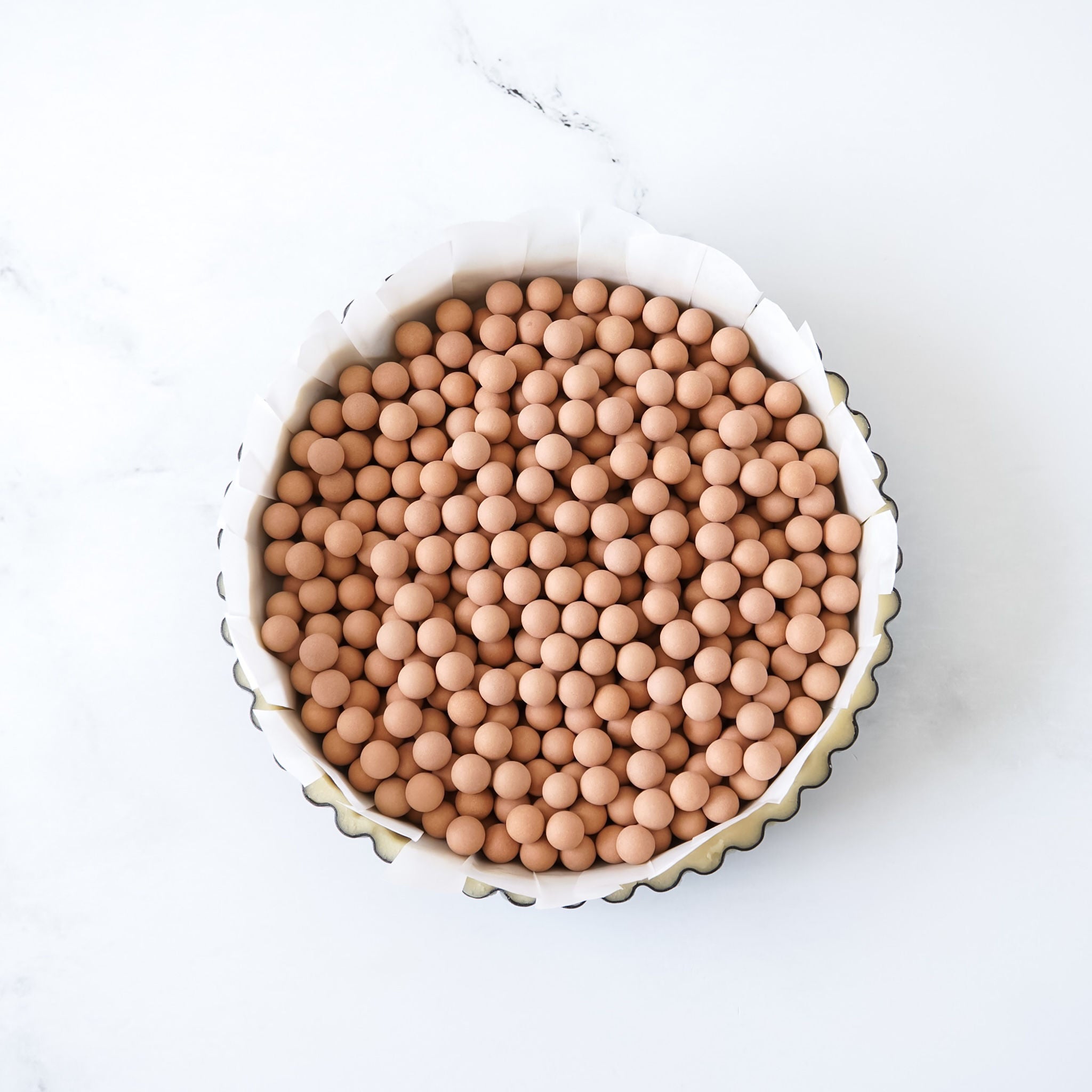 tart pan filled with red clay pie weights on a white background