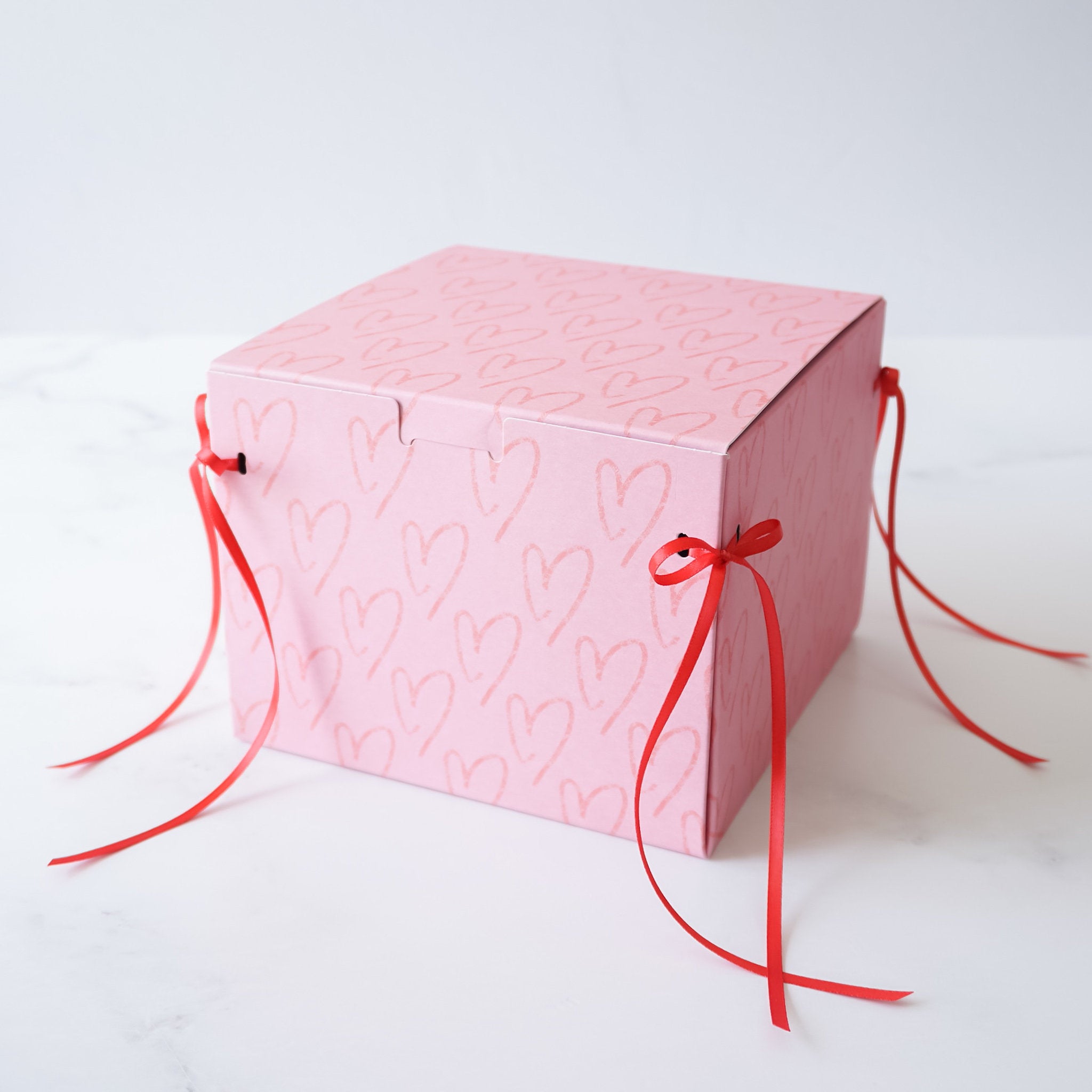 A heart-printed pink cookie box with red ribbon on a white background.
