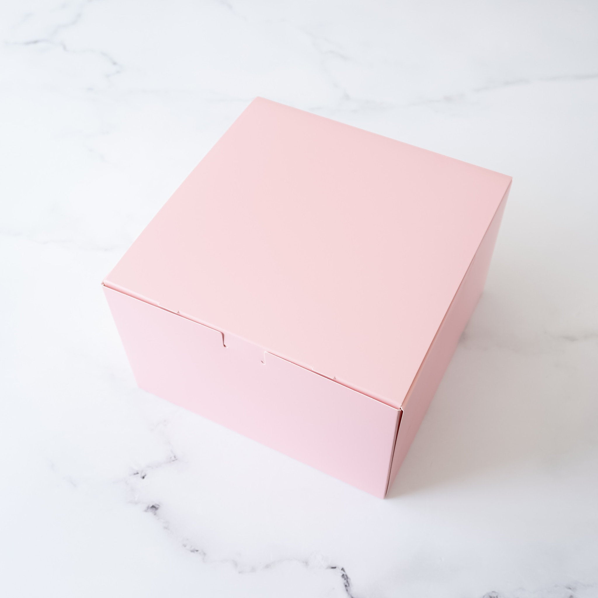 A pink square box with a plain surface and a flap on the top.