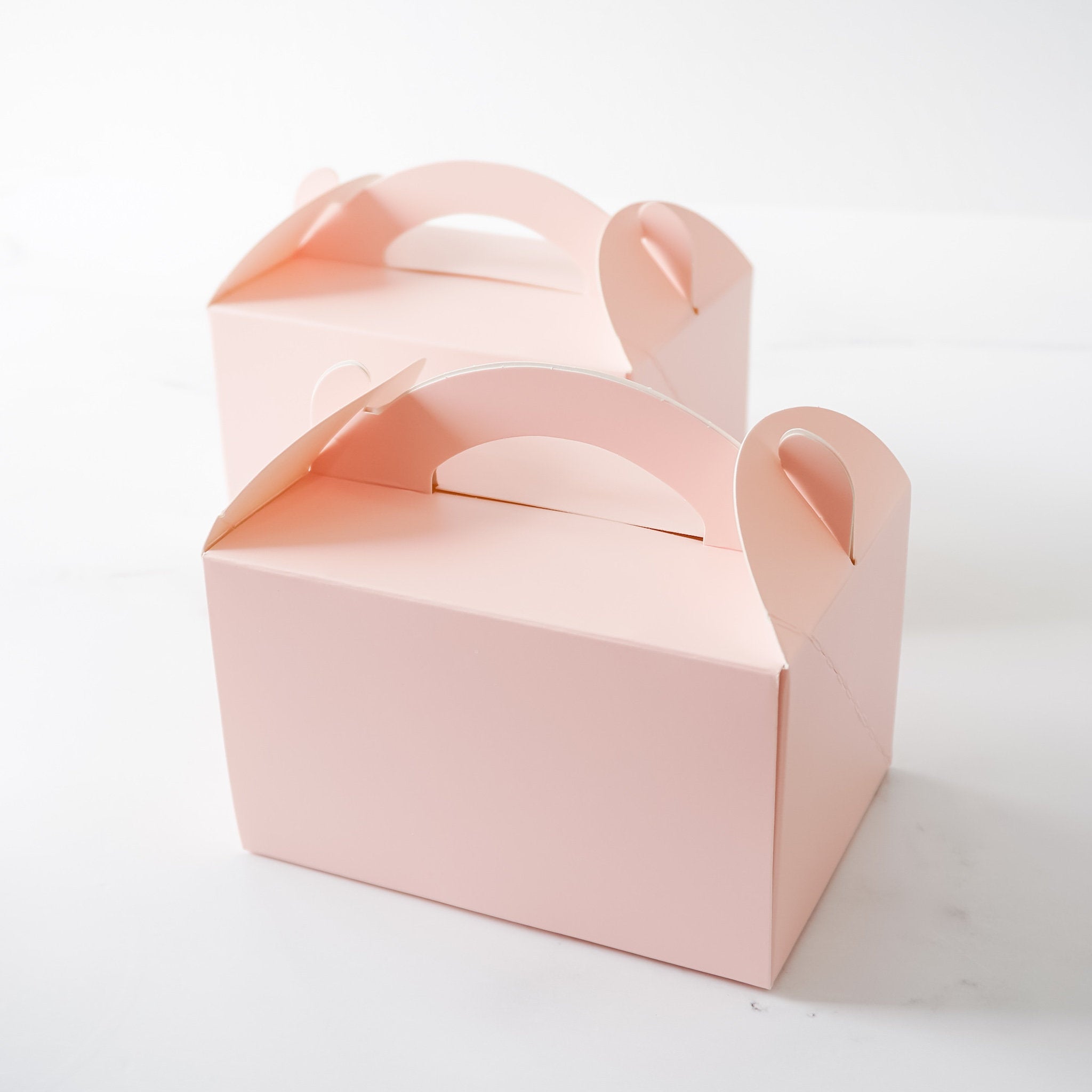 Two pink matte-coated gable boxes with handles, designed for baked goods.