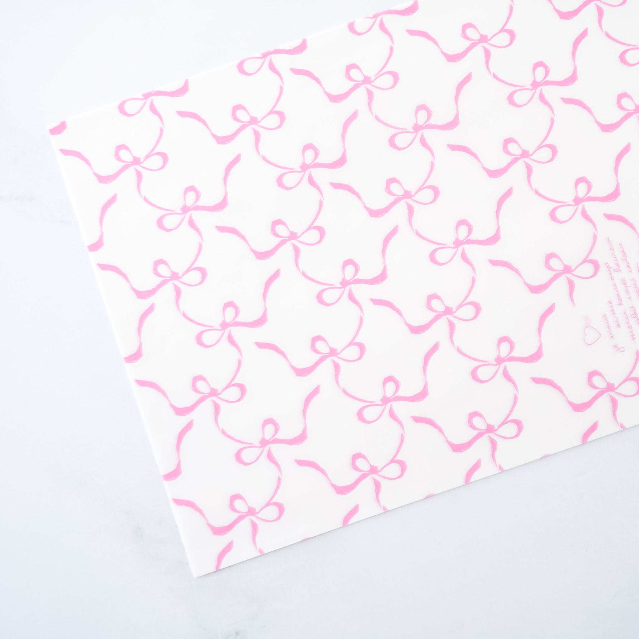 A sheet of white deli paper with pink ribbon bow print on a light background.