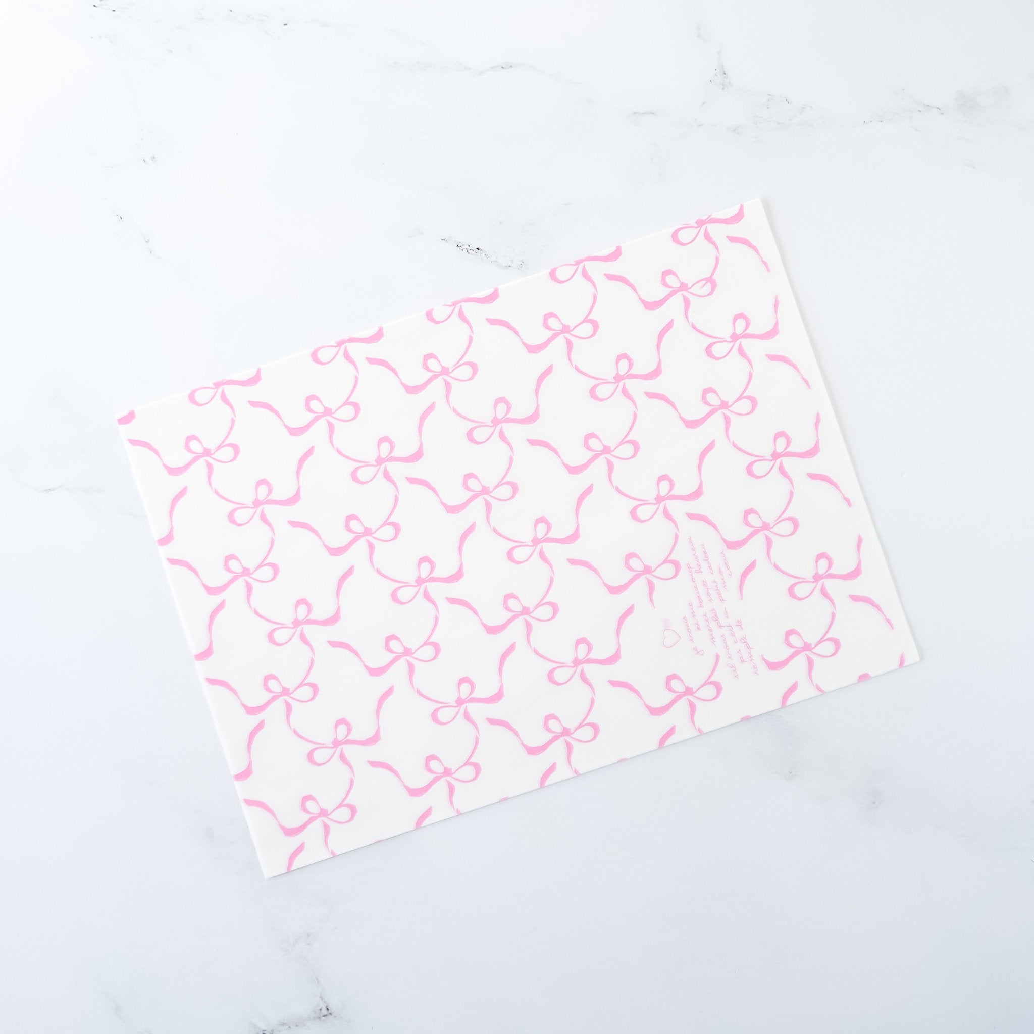 A sheet of white deli paper with pink ribbon bow print on a light background.
