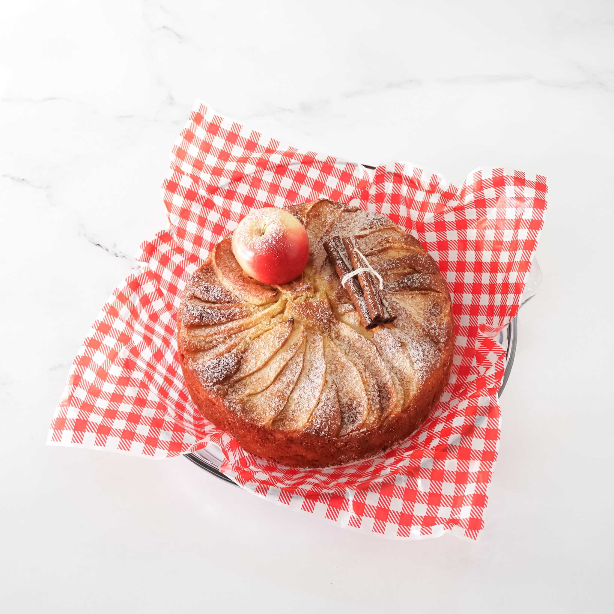Baked apple cake with a cinnamon stick on a red and white checkered deli paper