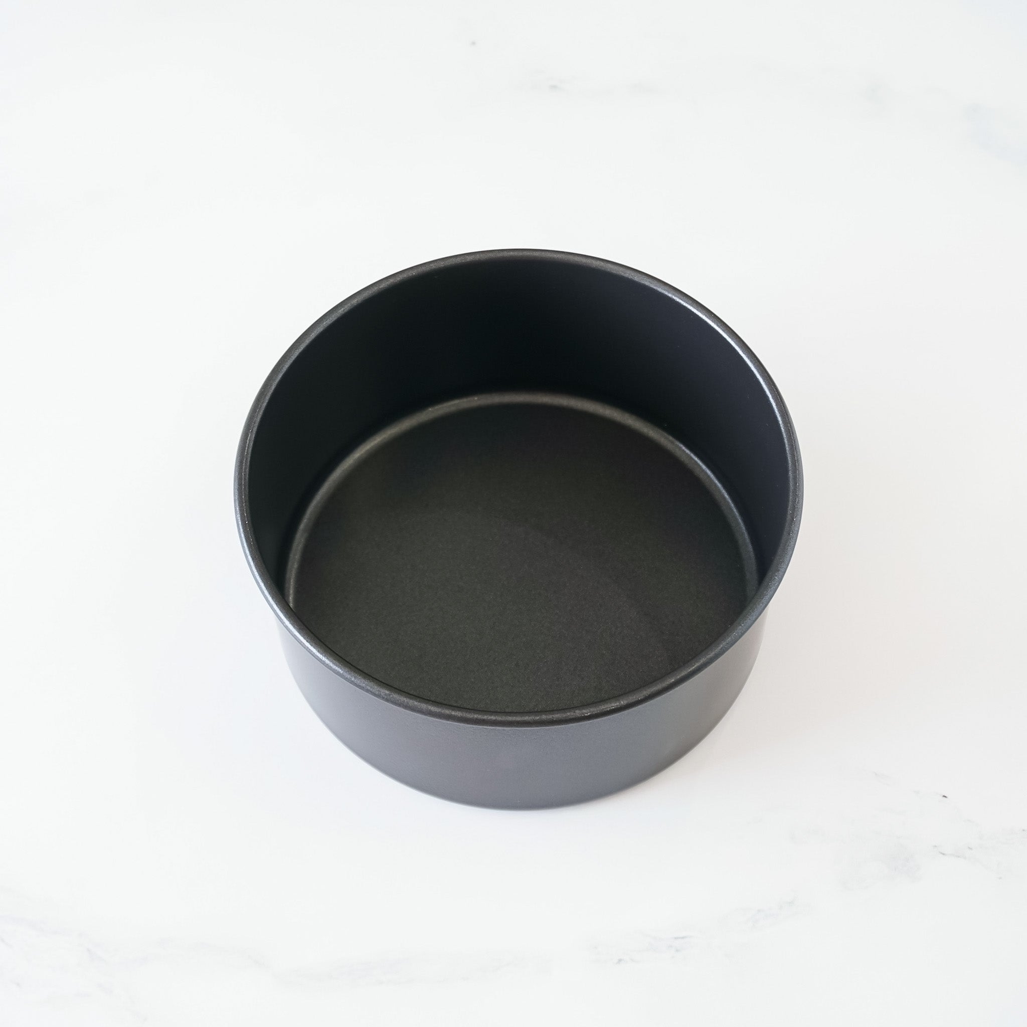 A round, black, nonstick cake pan with a smooth, shiny surface.