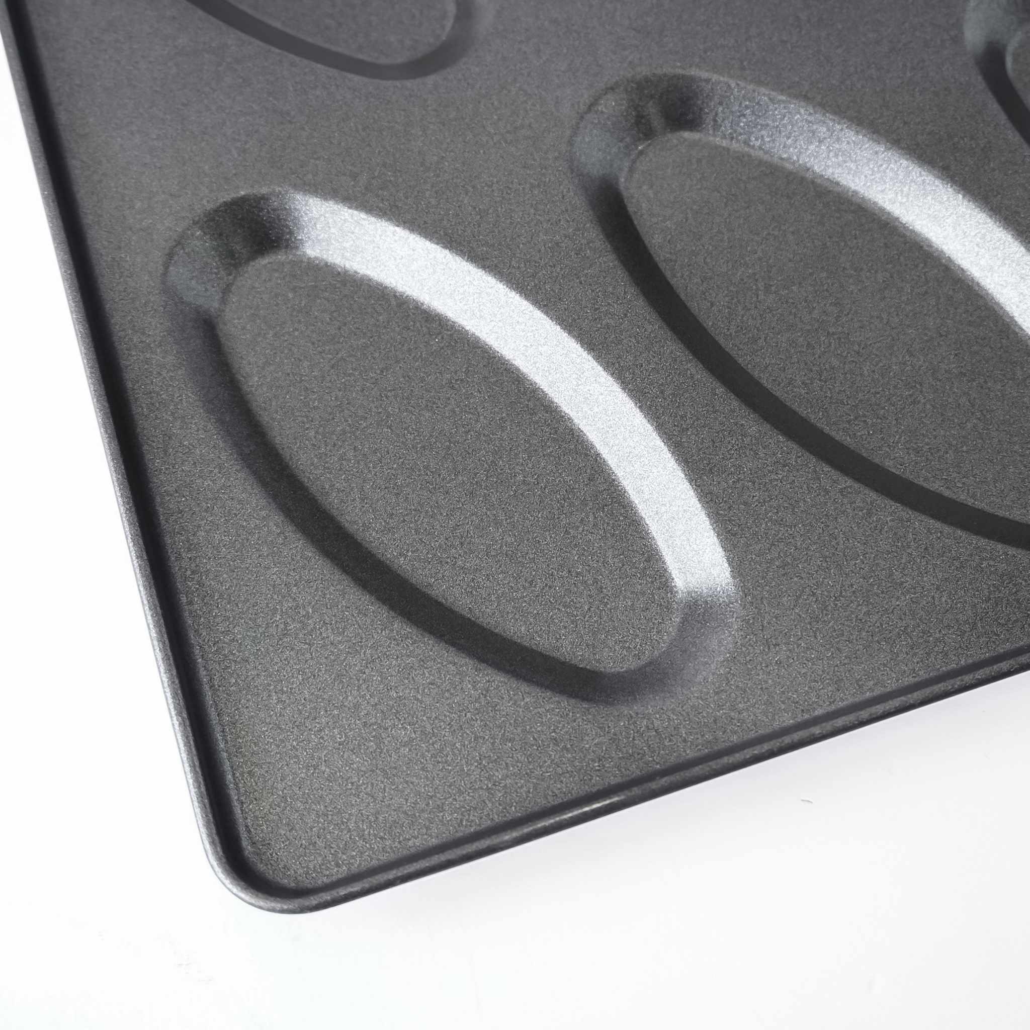 Close-up of a dark gray non-stick baking pan with oval-shaped molds, showing the textured surface and raised edges on a white background.