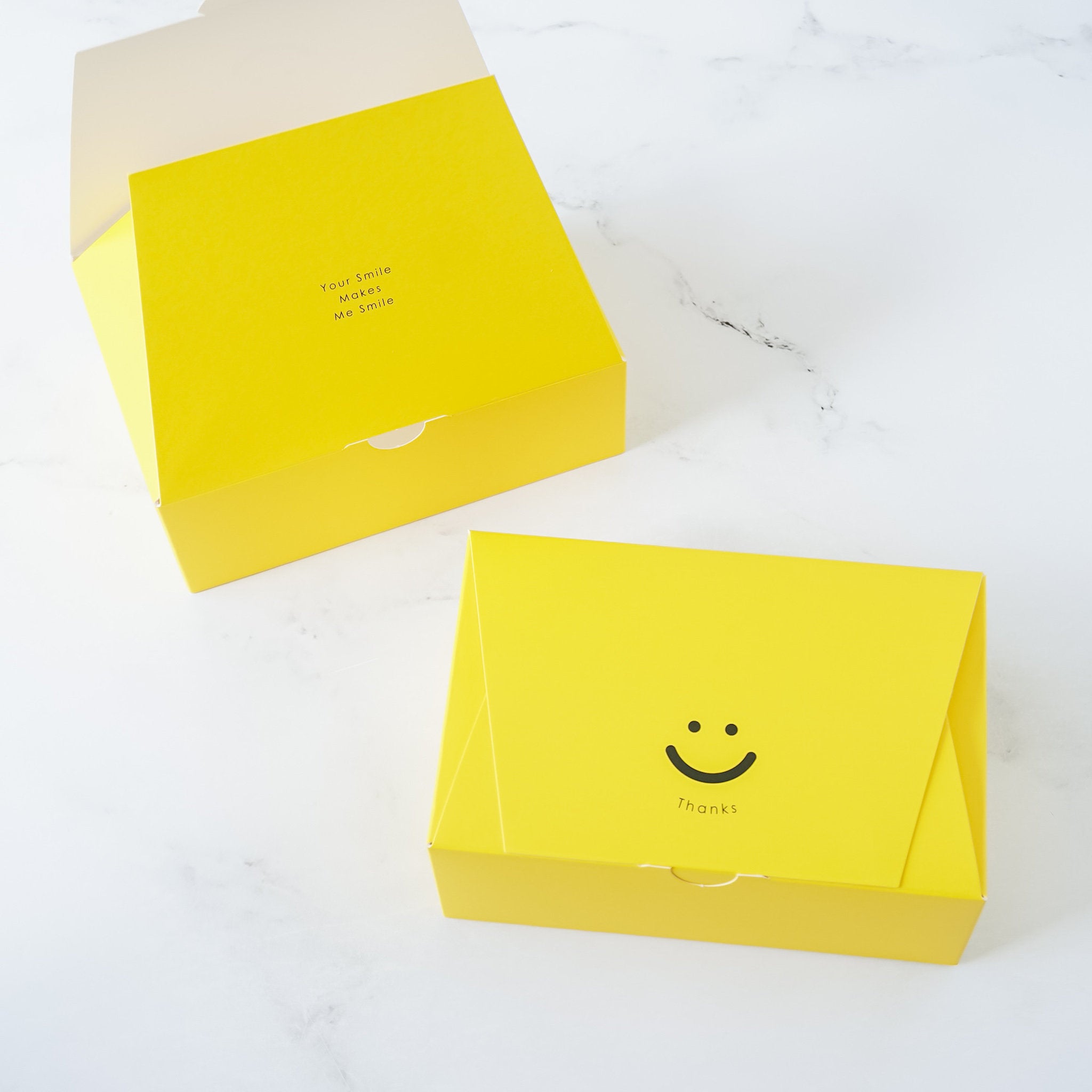 Two bright yellow cookie boxes with a smiley face design and a &