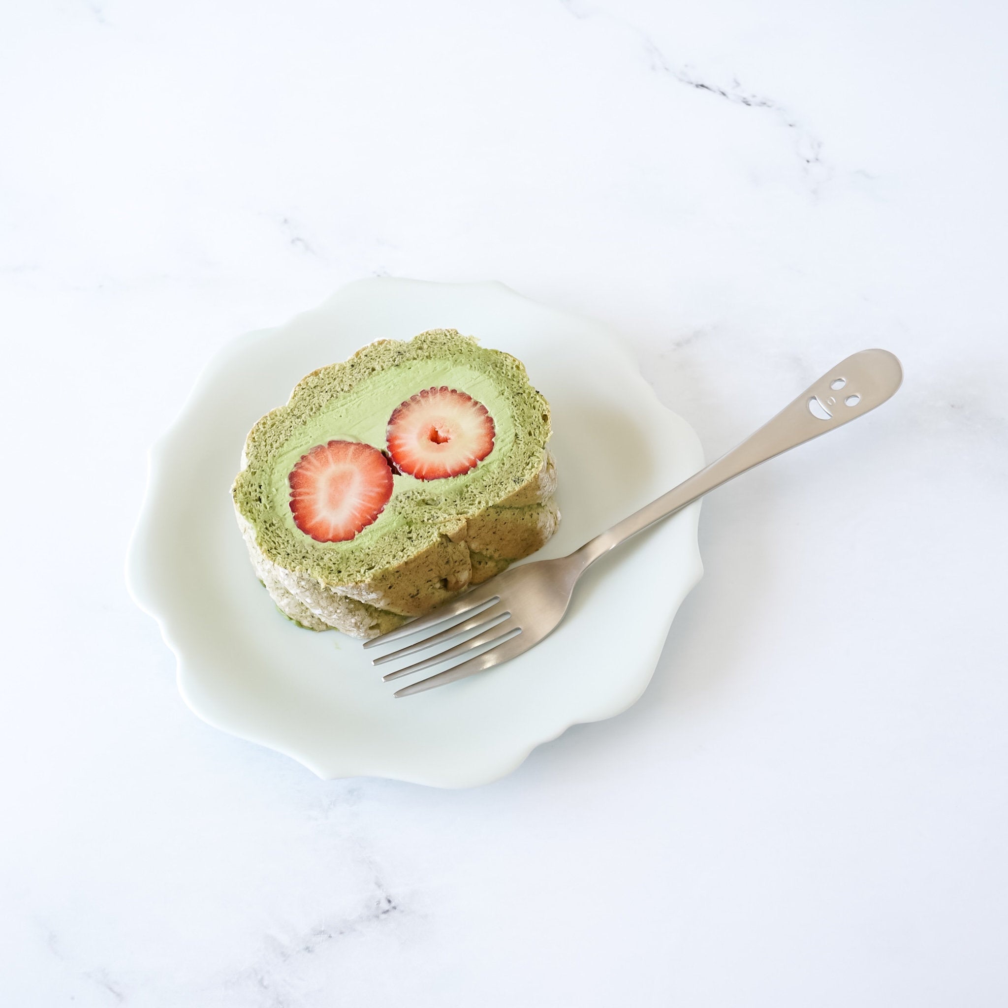 Slice of matcha roll cake with strawberries on a white plate with a fork.