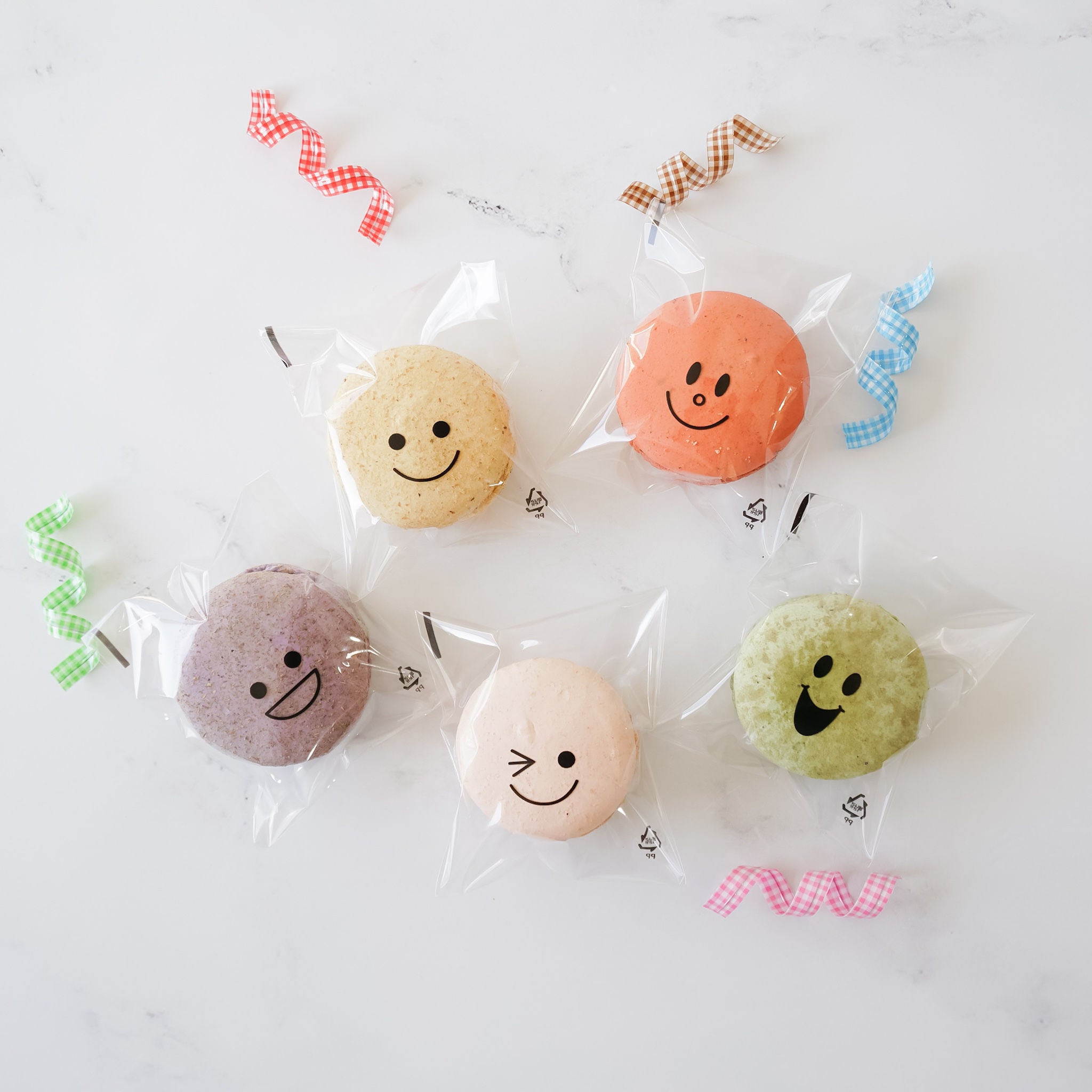Assorted smile printed cellophane bags containing various colored macarons, displayed on a white surface.