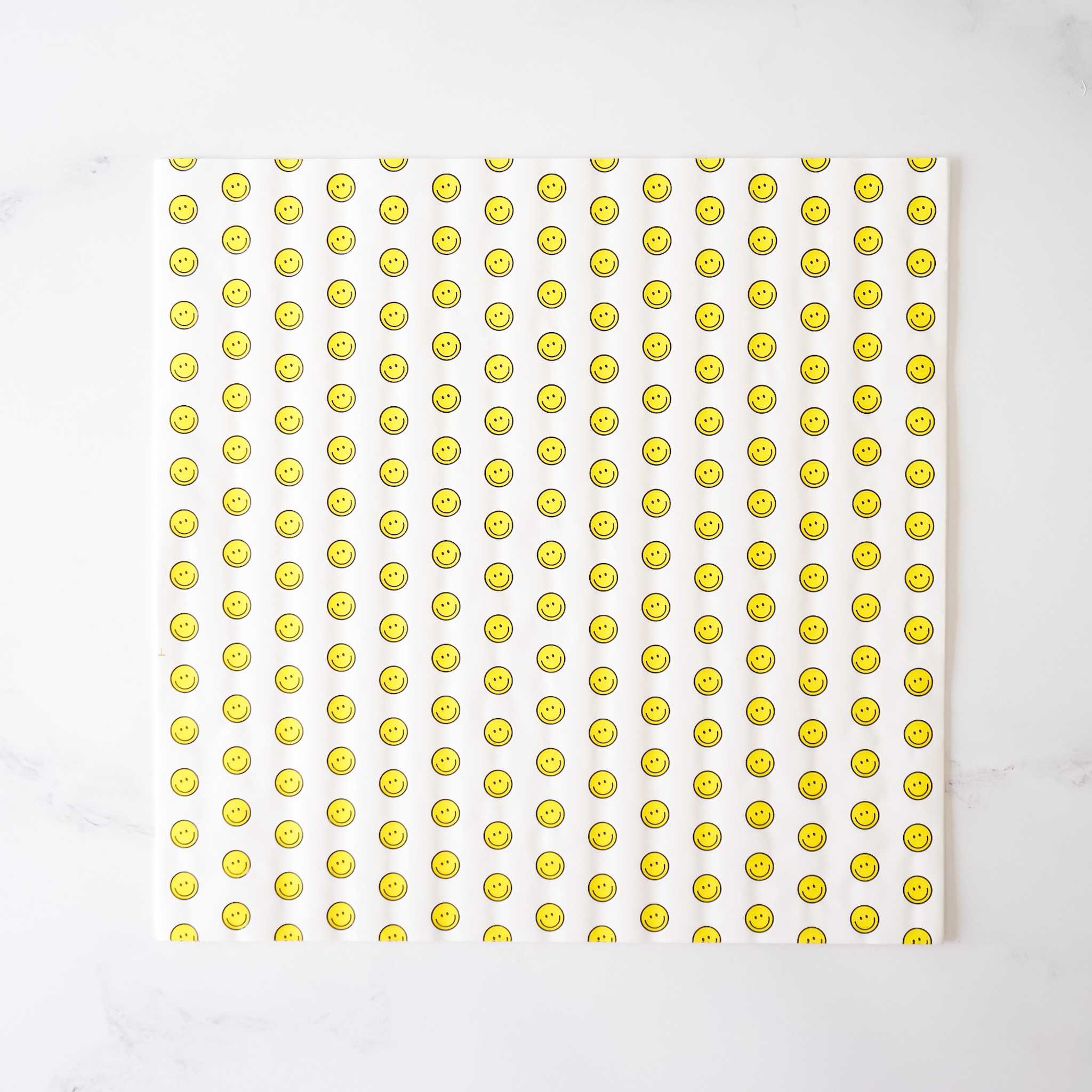 A sheet of deli paper with a yellow smiley face pattern on a white background, presumably made of coated parchment paper.
