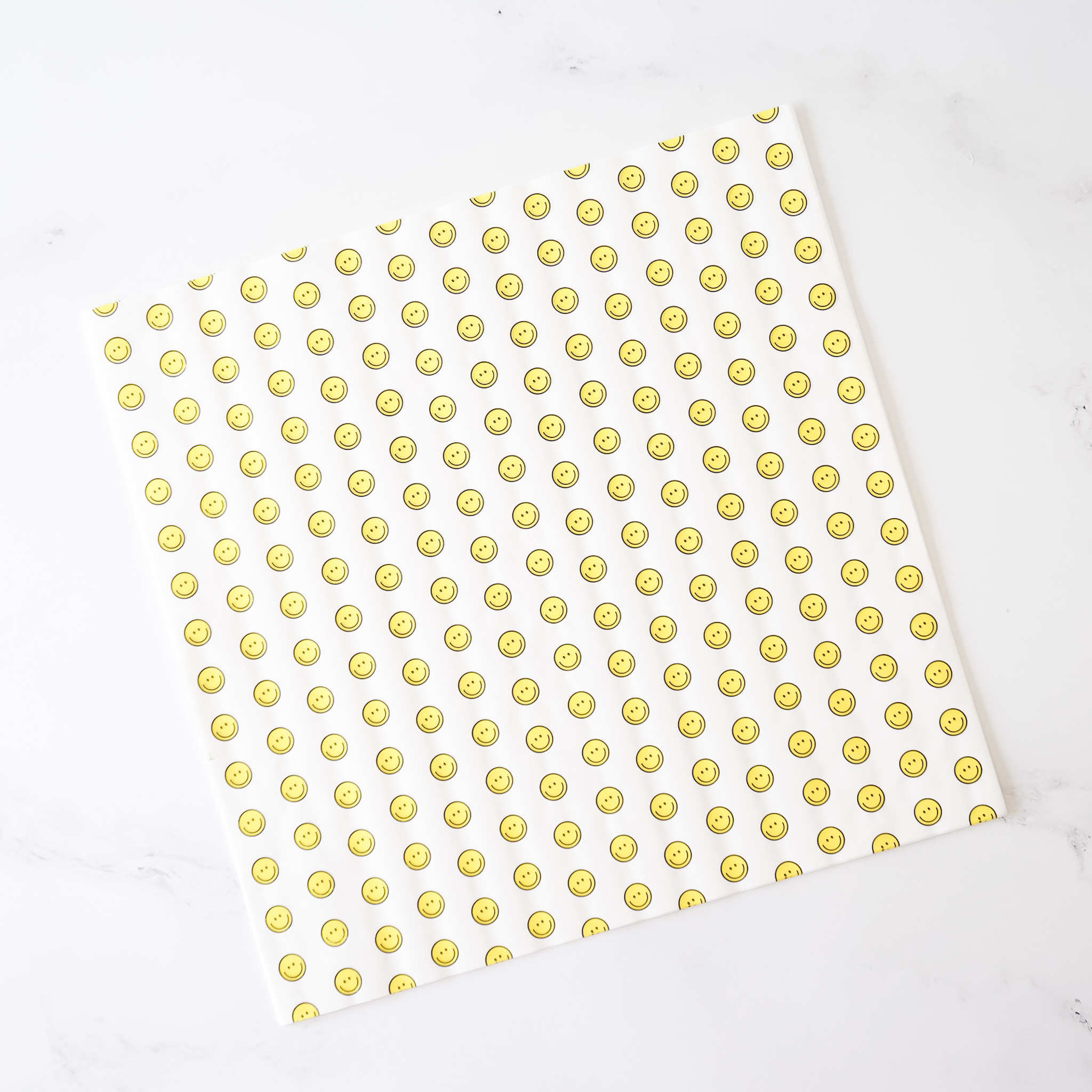 A sheet of deli paper with a yellow smiley face pattern on a white background, presumably made of coated parchment paper.
