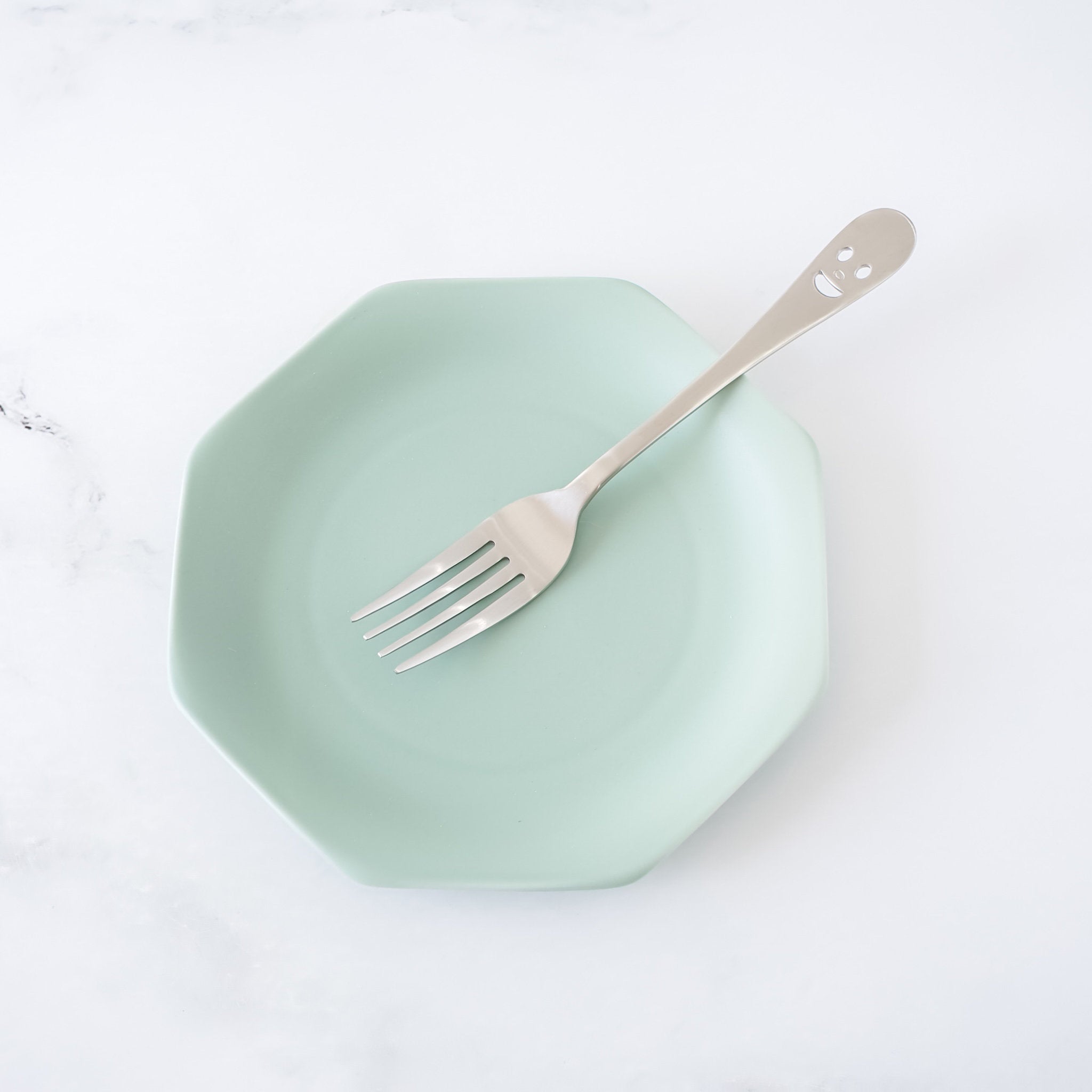 Mint green plate with a fork on a white background