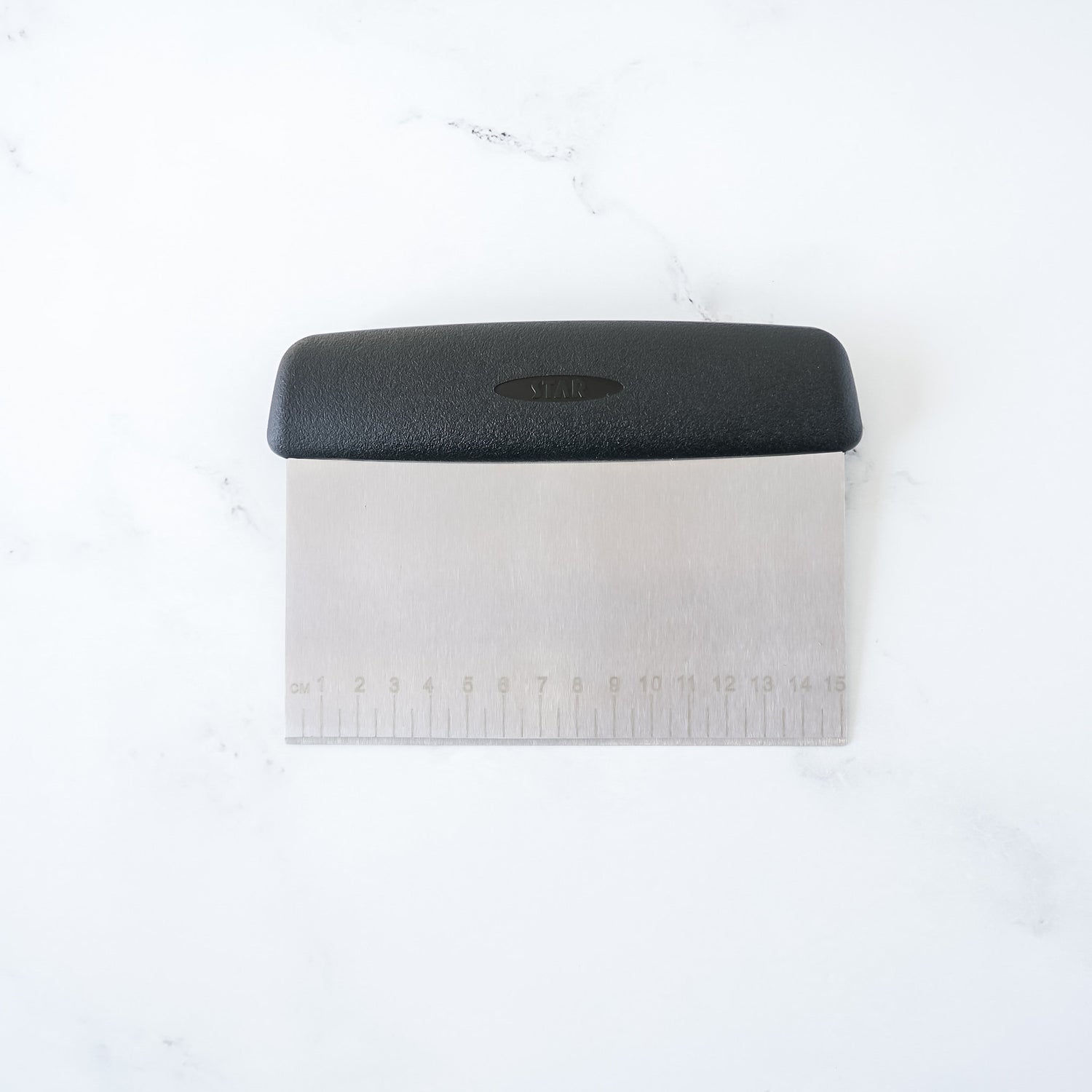 A stainless steel bench scraper with a black non-slip handle and 0.5 cm measurement markings on the blade.