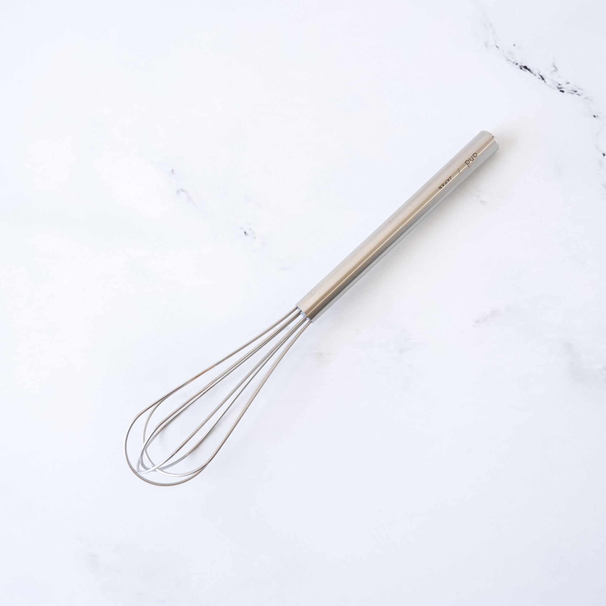 stainless steel mini whisk with slim handle on a white marble surface