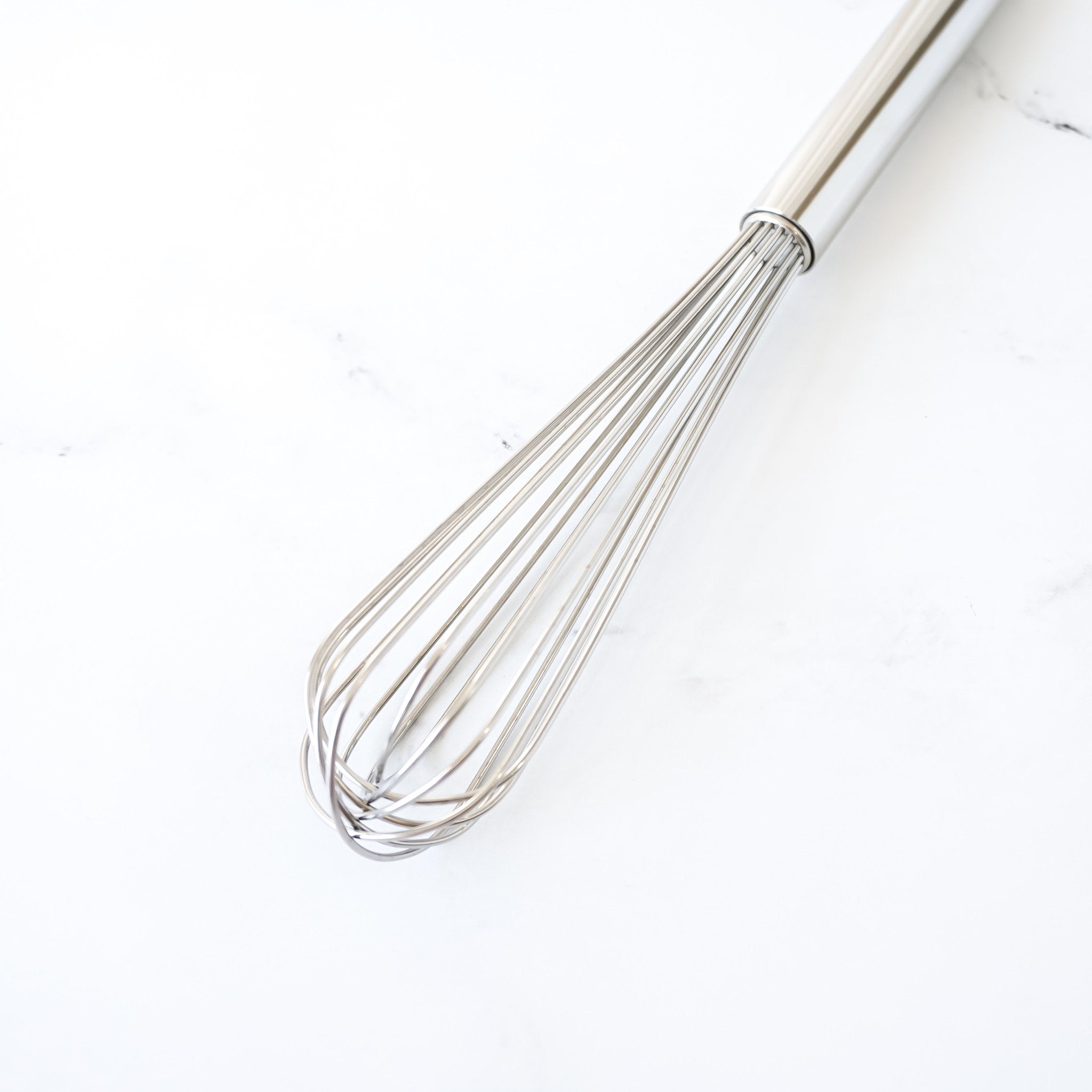 A stainless steel slim wire whisk on a white background.