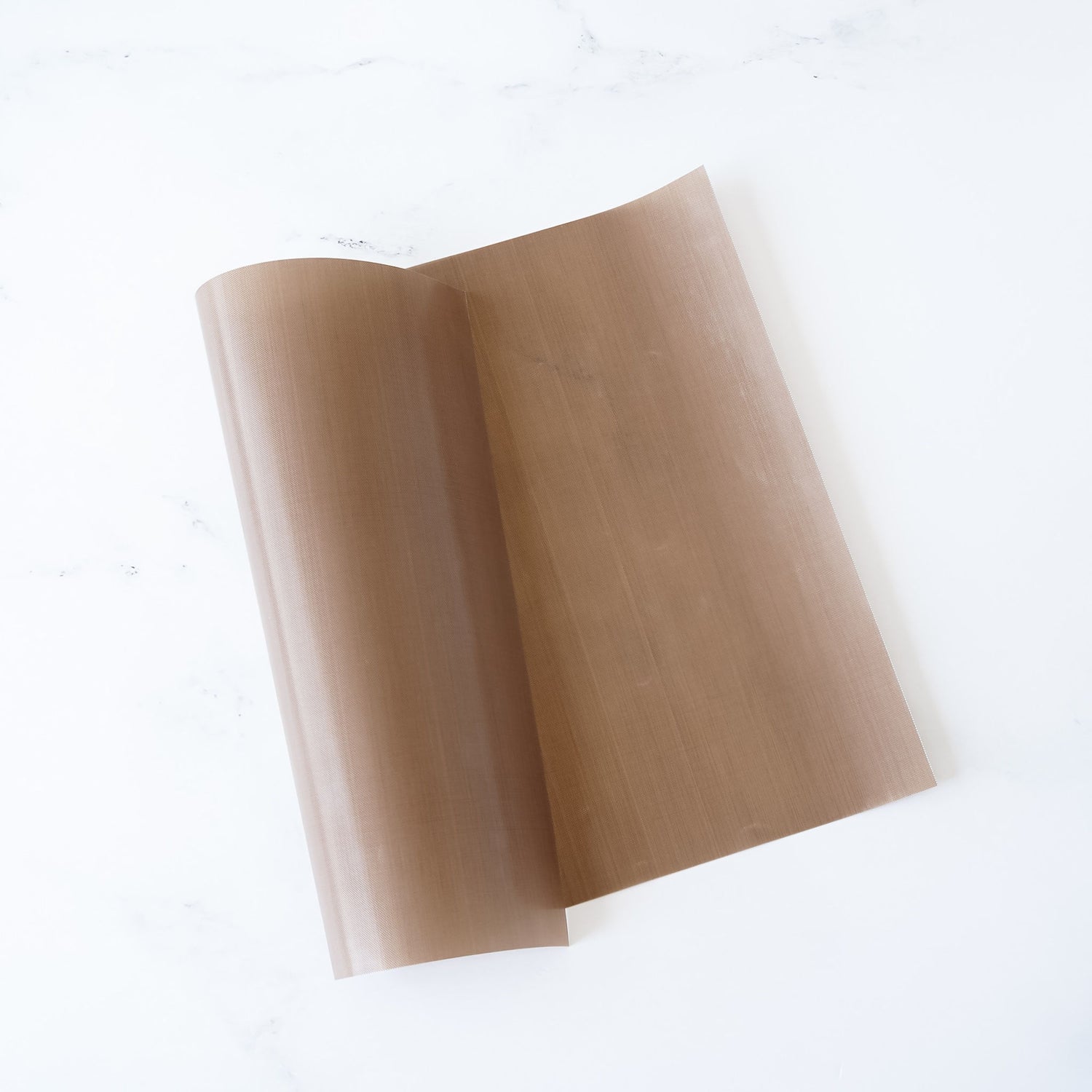 A Teflon sheet with a non-stick surface, beige in color, rolled up at one end, placed on a white background.