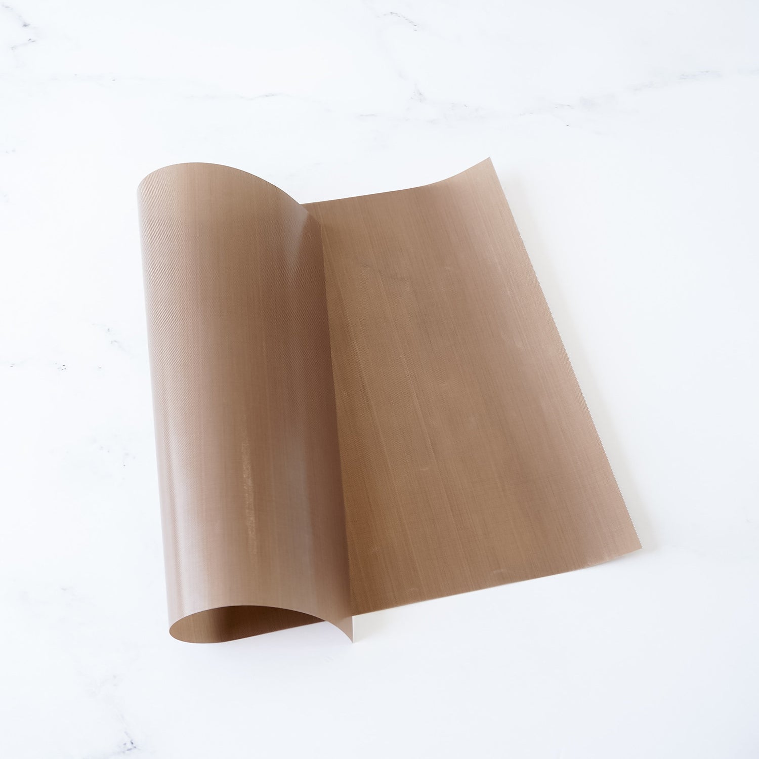 A Teflon sheet with a non-stick surface, beige in color, rolled up at one end, placed on a white background.