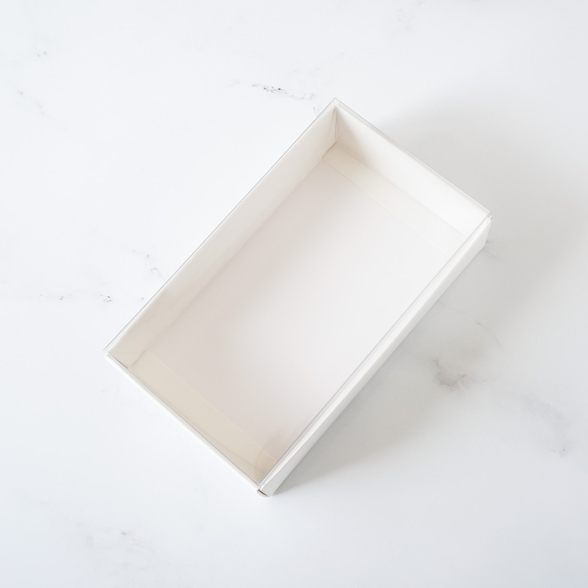 A white rectangular box with a lid open, revealing an empty interior. The box is made of cardboard and has a smooth, matte finish.