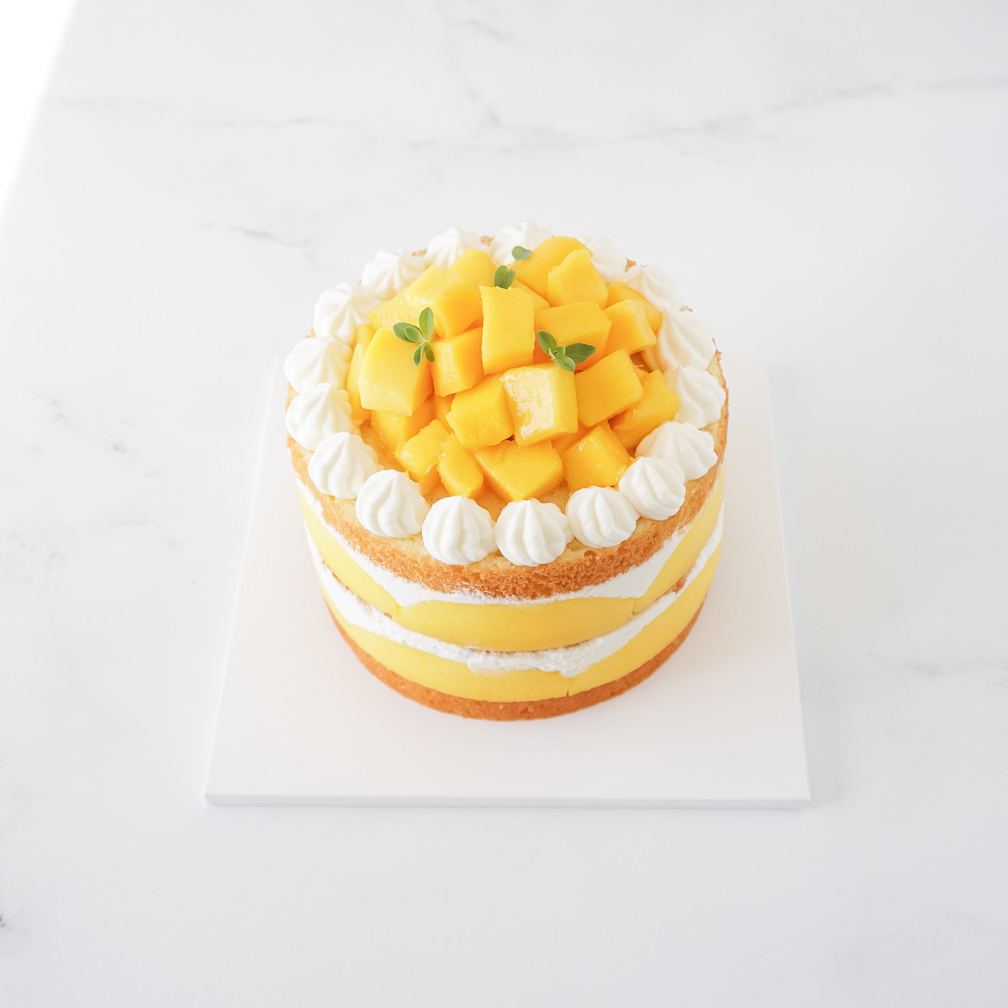 A mango cake presented on a white square cake board with a matte finish.