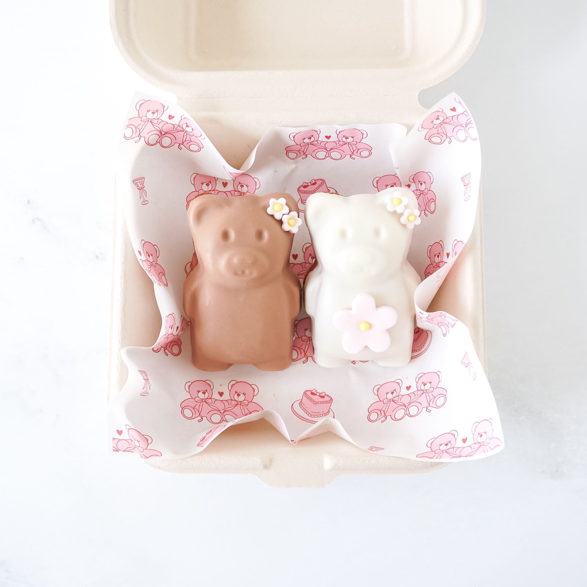 Two small bear-shaped madeleines in a decorative box with pink teddy bear pattern on a white background