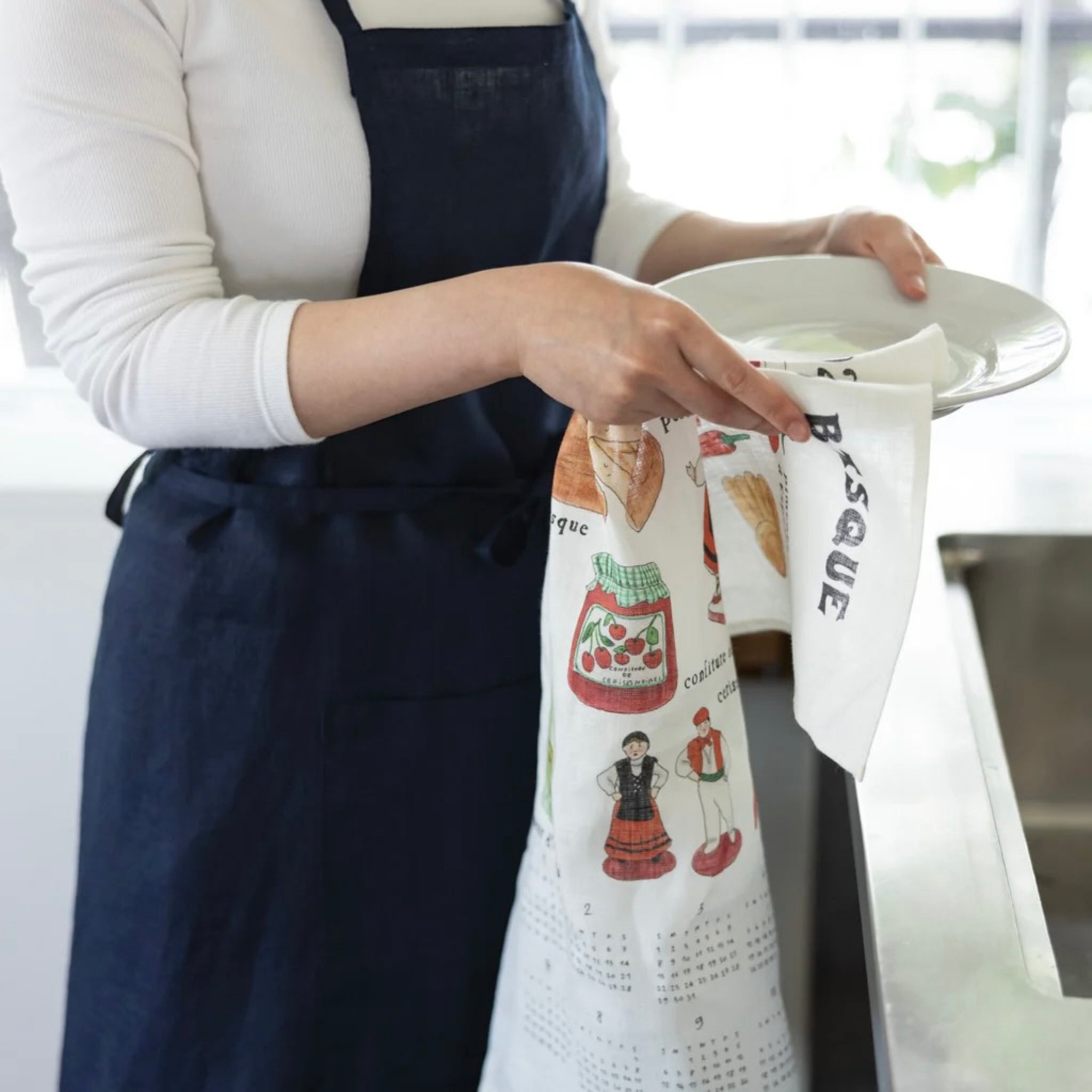Person holding a white dish with a decorative towel featuring illustrations and text.