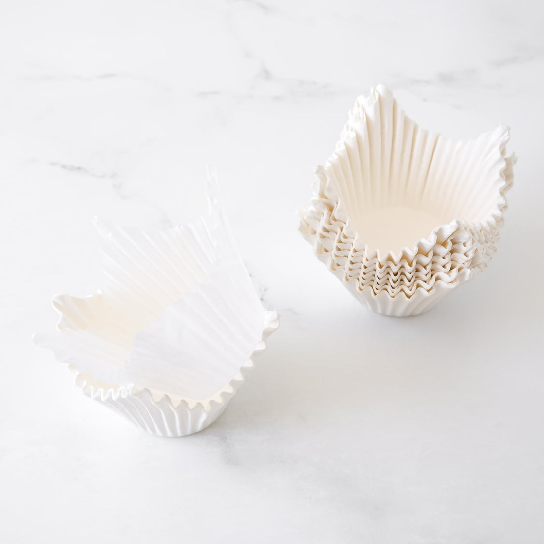 Two white cupcake liners with scalloped edges on a light gray background