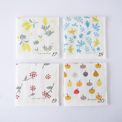 Four square fabric dishcloths with different autumn-themed prints, arranged in a 2x2 grid on a white background. The prints feature yellow flowers, blue leaves, red berries, and pumpkins on an off-white base.