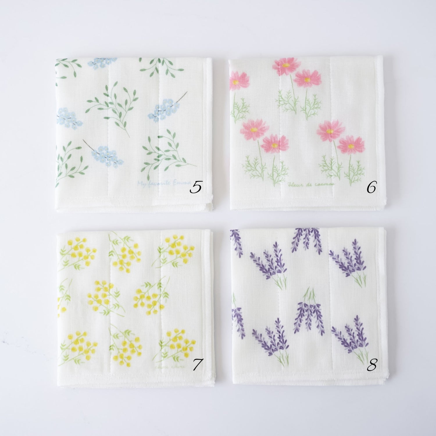 Four square white fabric kitchen cloths with different floral prints arranged in a 2x2 grid on a white background. The top-left cloth has blue flowers and green leaves, the top-right has pink flowers, the bottom-left has yellow flowers, and the bottom-right has purple lavender sprigs.