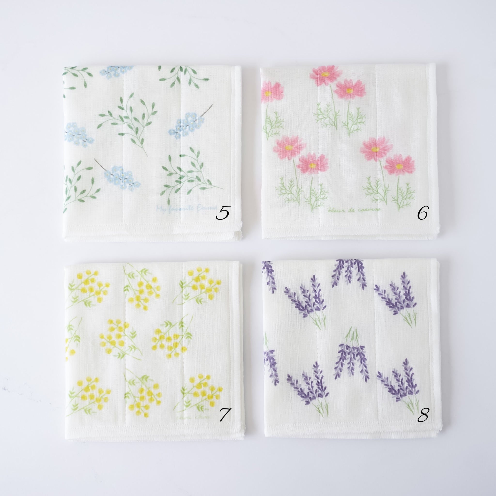 Four square white fabric kitchen cloths with different floral prints arranged in a 2x2 grid on a white background. The top-left cloth has blue flowers and green leaves, the top-right has pink flowers, the bottom-left has yellow flowers, and the bottom-right has purple lavender sprigs.