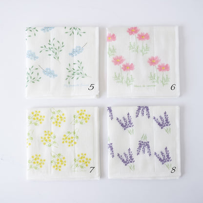 Four square white fabric kitchen cloths with different floral prints arranged in a 2x2 grid on a white background. The top-left cloth has blue flowers and green leaves, the top-right has pink flowers, the bottom-left has yellow flowers, and the bottom-right has purple lavender sprigs.