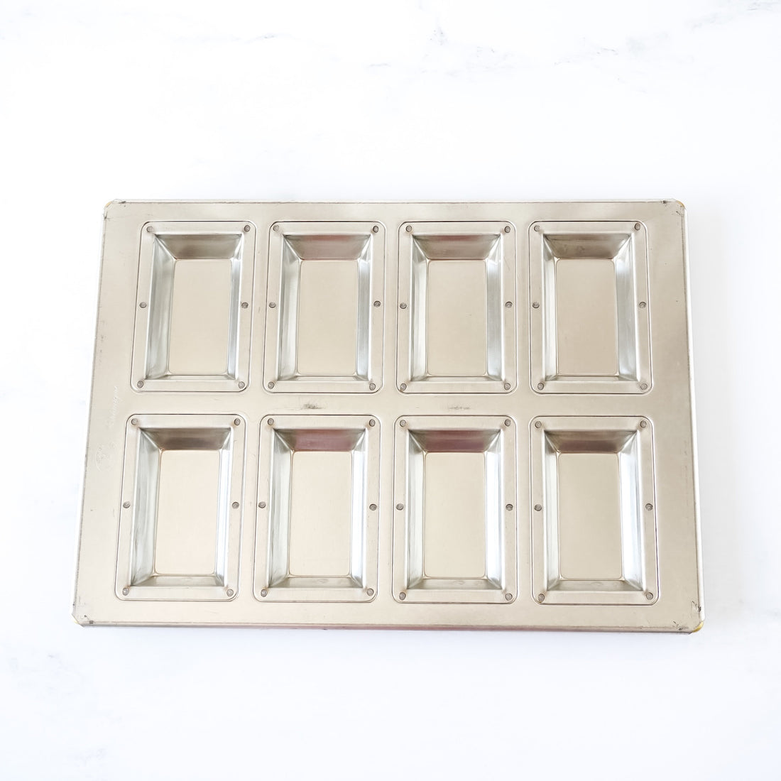 Silicone-coated metallic financier pan with eight square compartments on a white background