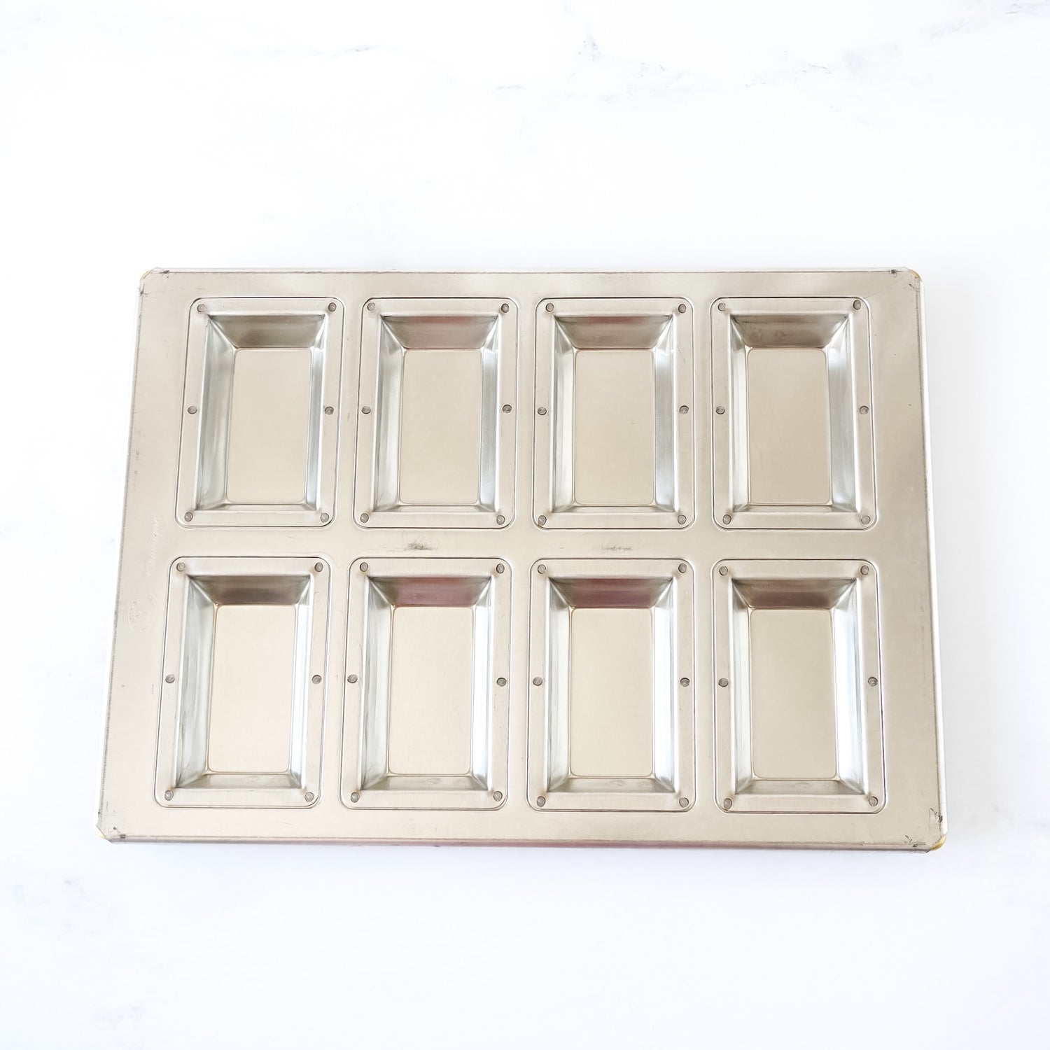 Silicone-coated metallic financier pan with eight square compartments on a white background