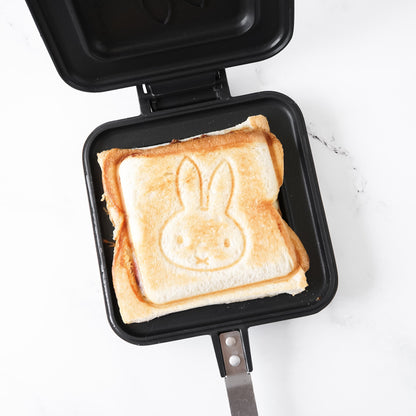 A hot sandwich maker with an open lid displaying a golden-brown sandwich with a Miffy character design on one side. The maker has a black body with a stainless steel handle.