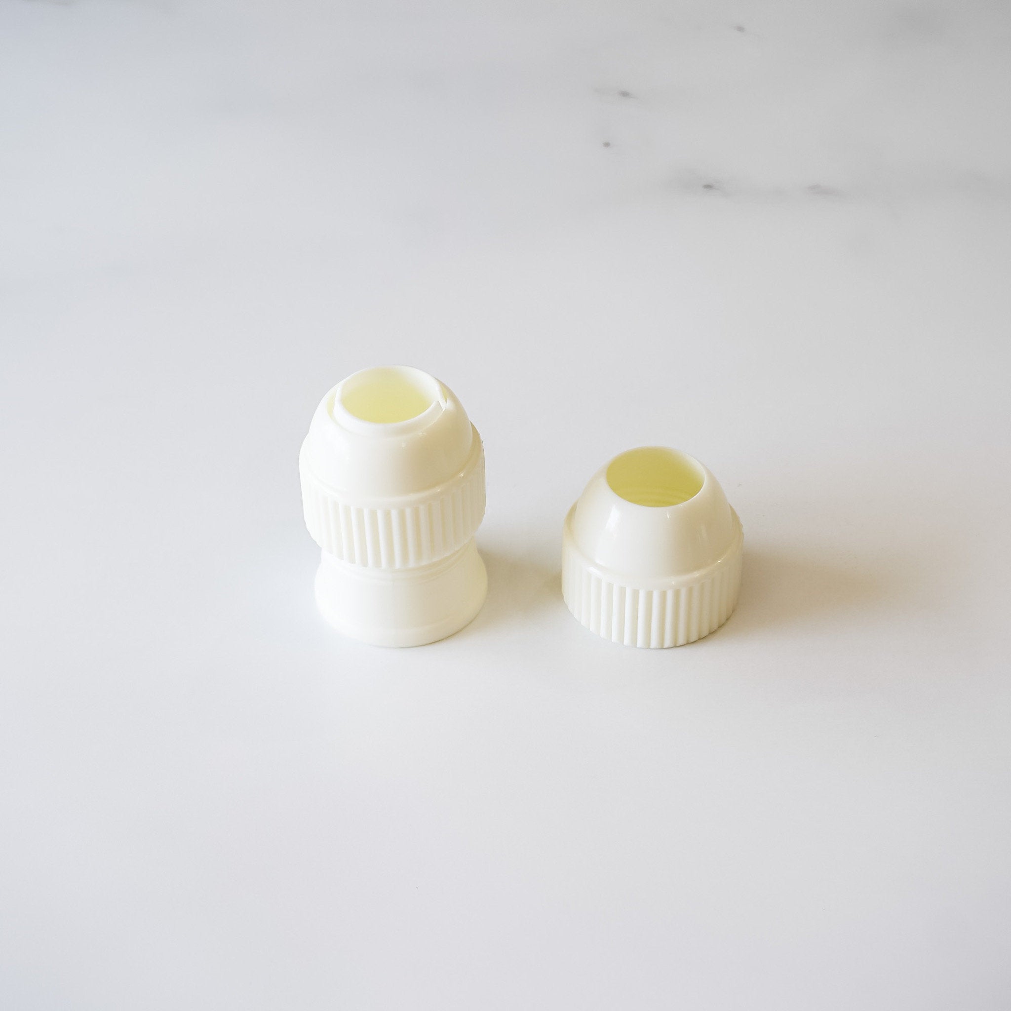 Two pieces of a white plastic coupler designed for medium-sized piping tips, displayed on a marble surface.