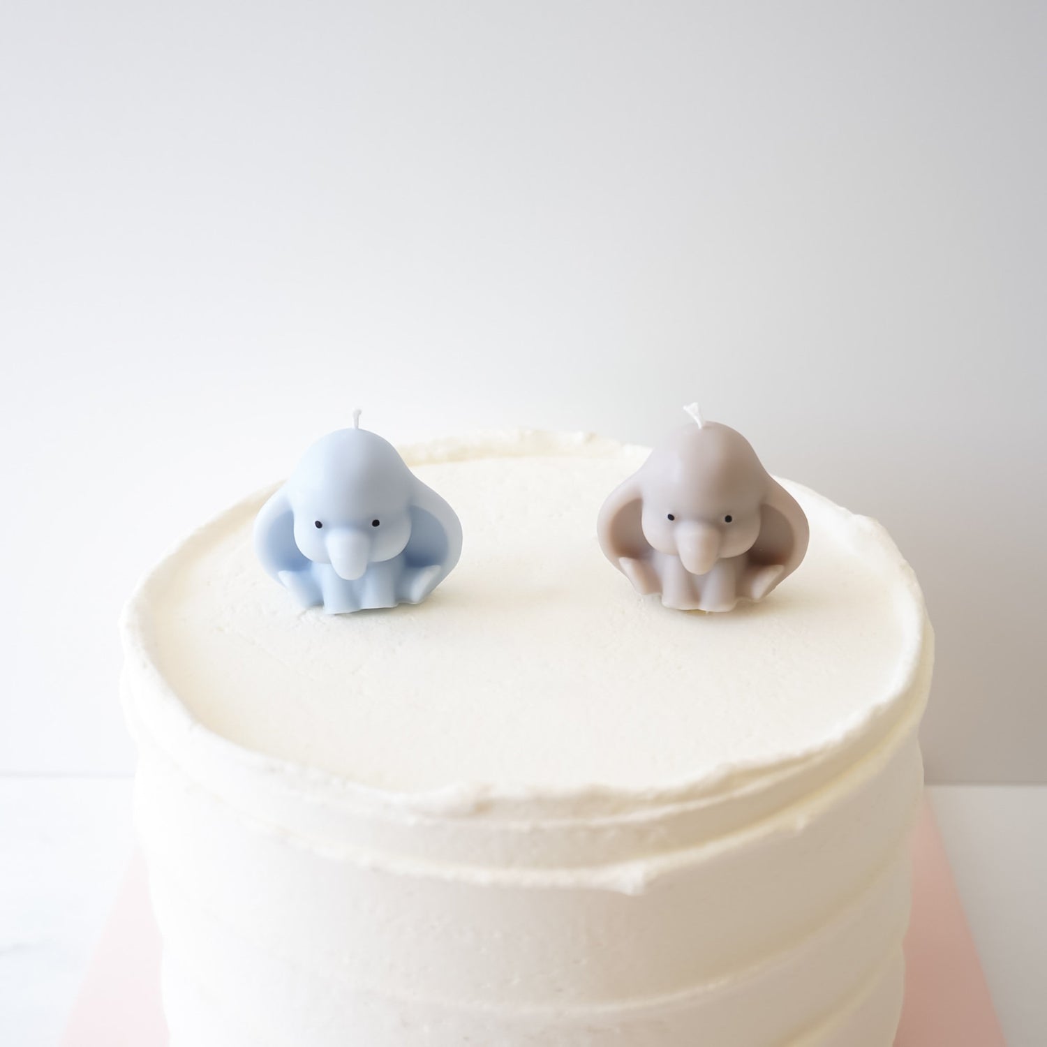 Two elephant cake toppers on a white cake against a light gray background
