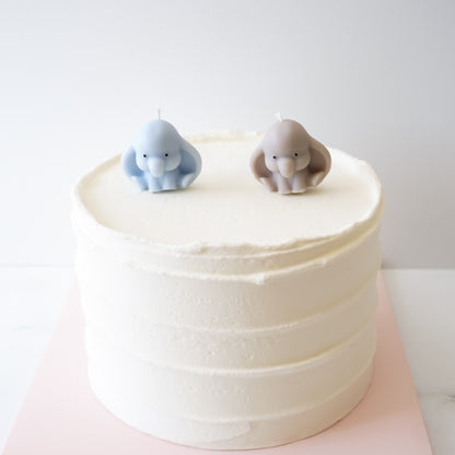 White cake with two elephant-shaped candles on a white background