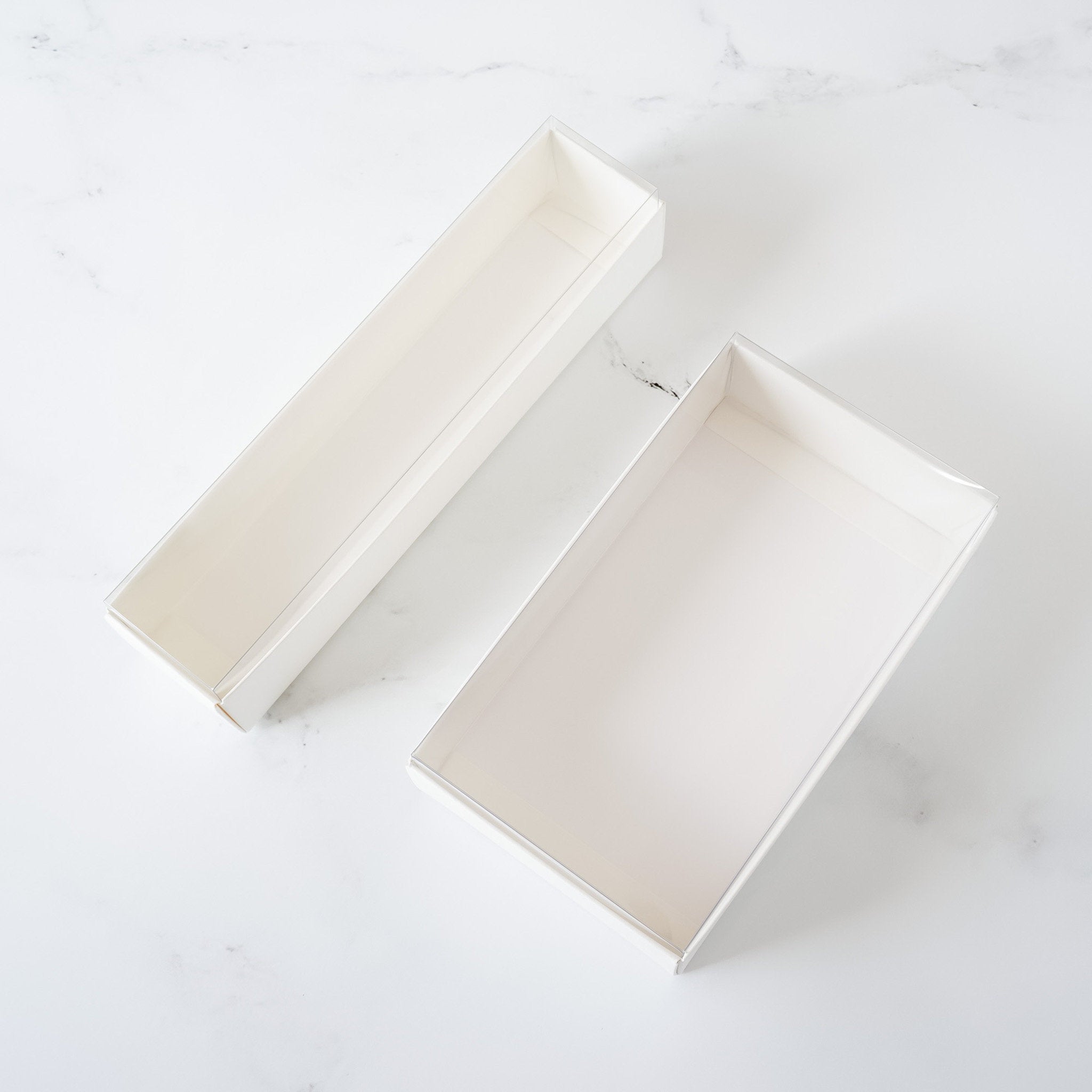 Two white cardboard boxes, one is a long rectangular box and the other is a square box. Both boxes are open and empty.