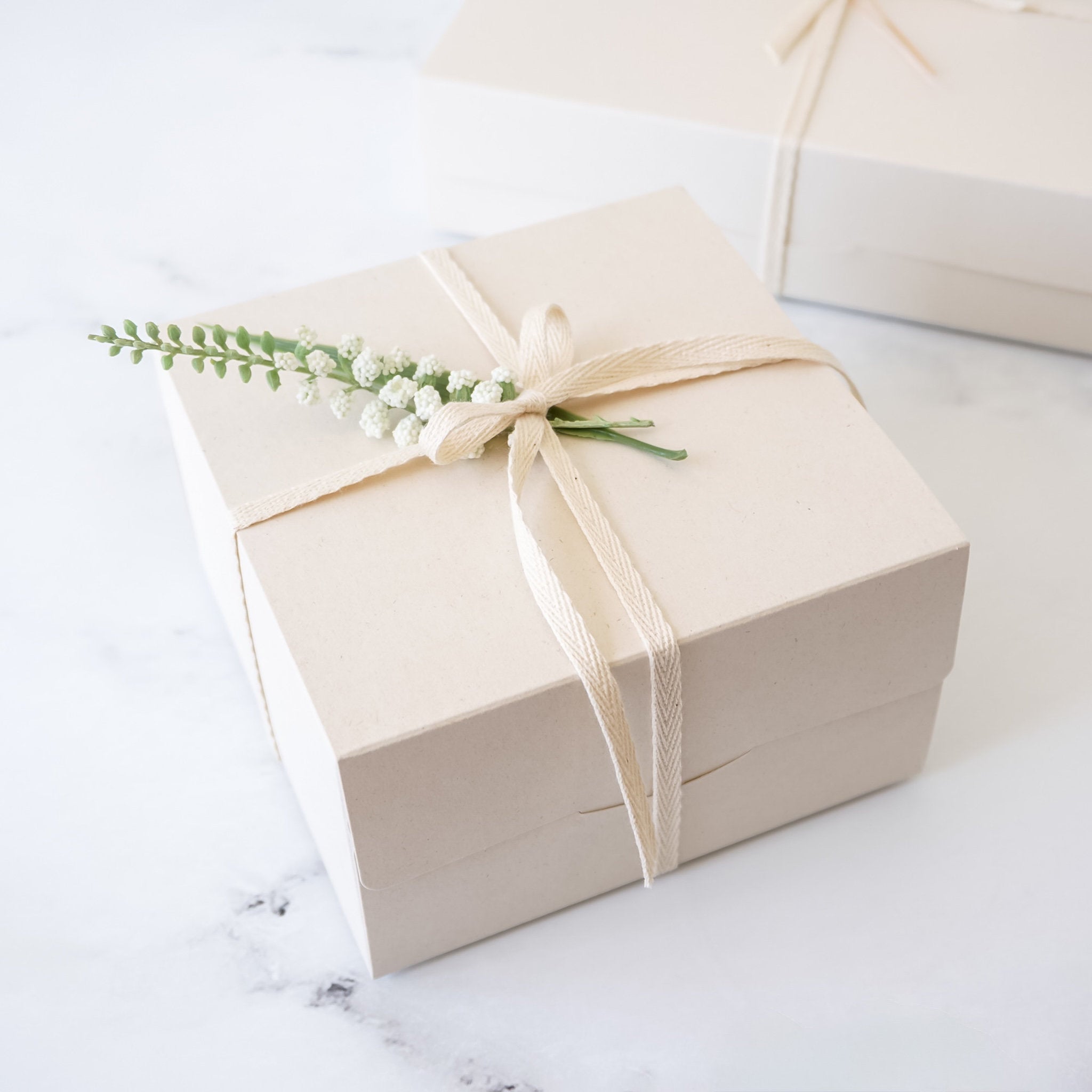 Beige gift box with a decorative bow and flowers on a light background