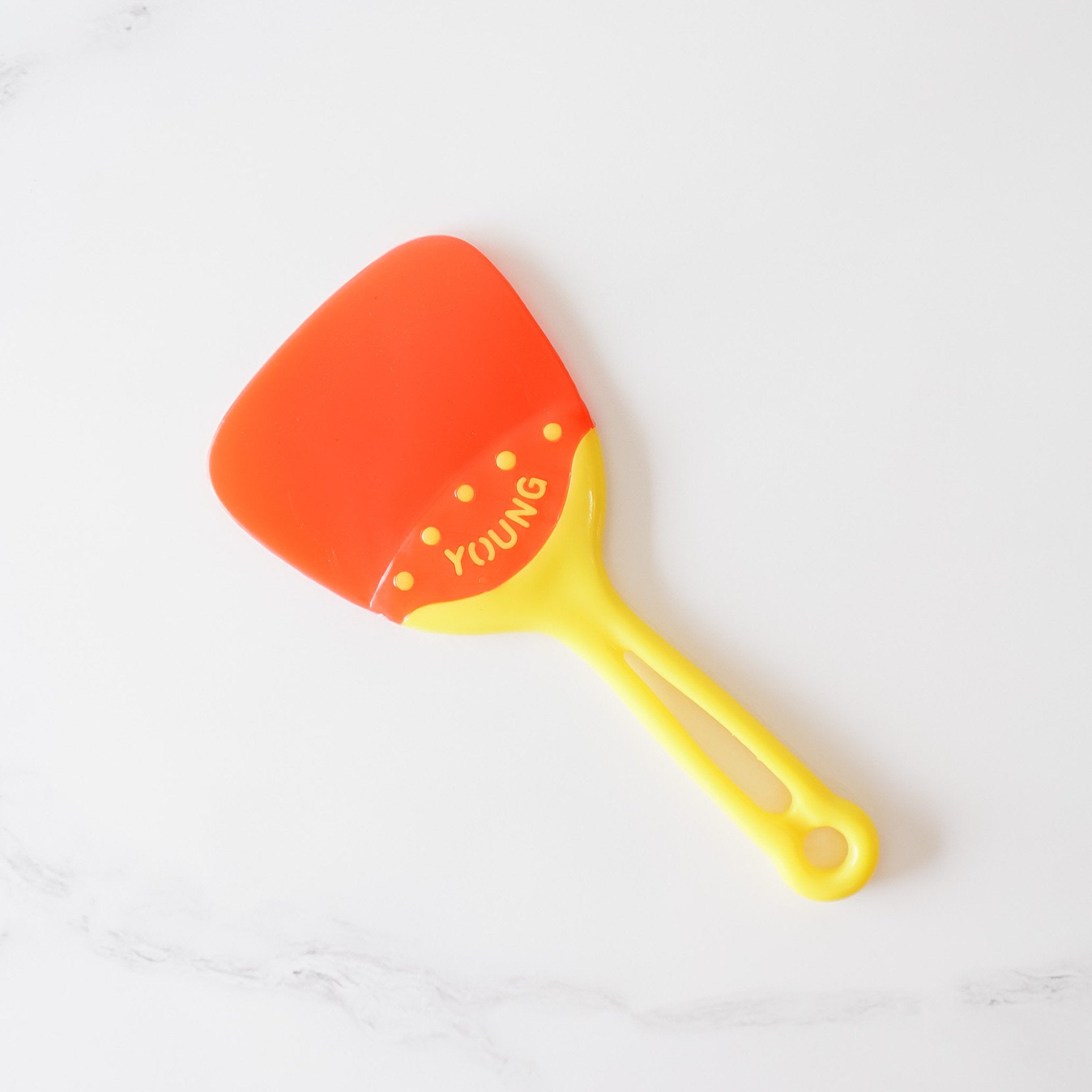A vibrant red and yellow plastic spatula features a unique, slightly curved, triangular shape.  The handle is yellow with a comfortable grip and a small hole at the end for hanging. The word &